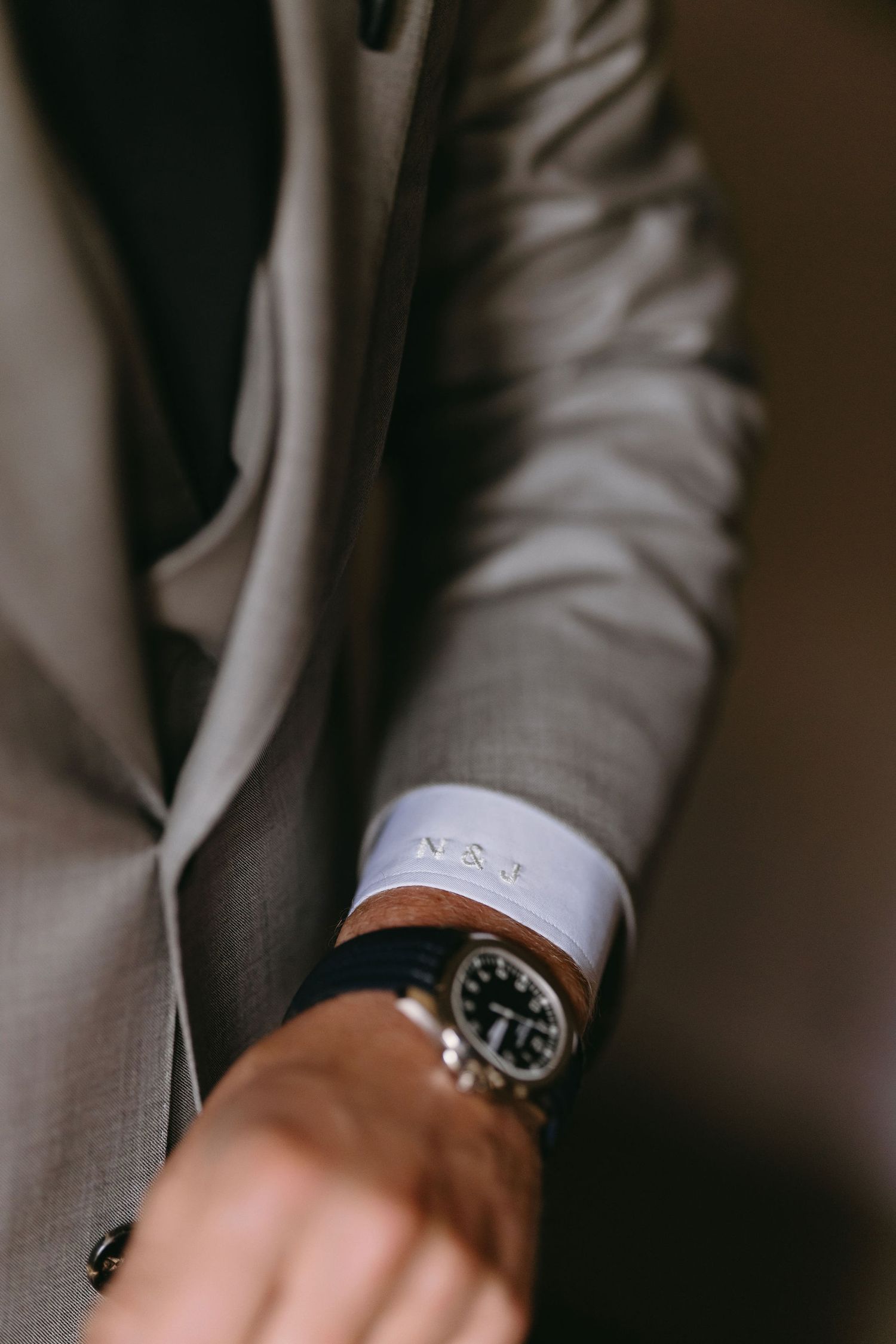 Close-up detail of a groom's gray suit sleeve with a luxury watch.