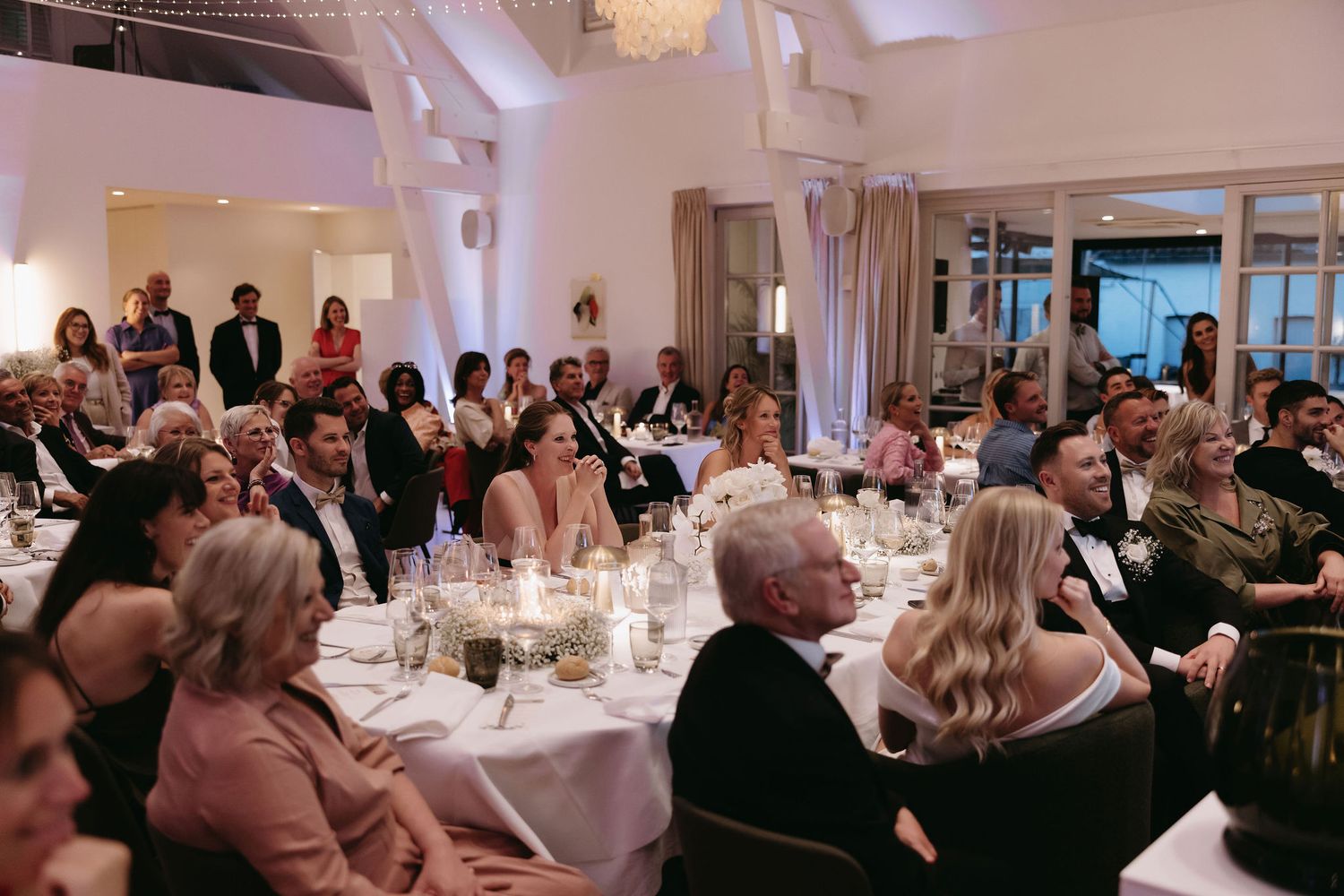 Wedding reception banquet hall filled with guests at decorated round tables.