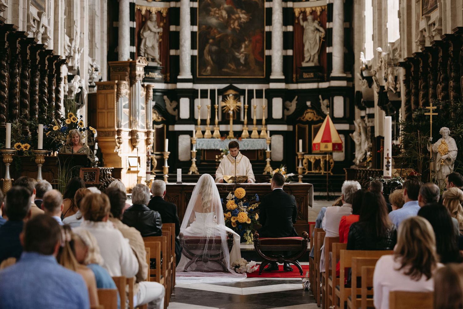 Wedding ceremony taking place in an ornate baroque church with gold decorations and high ceilings.