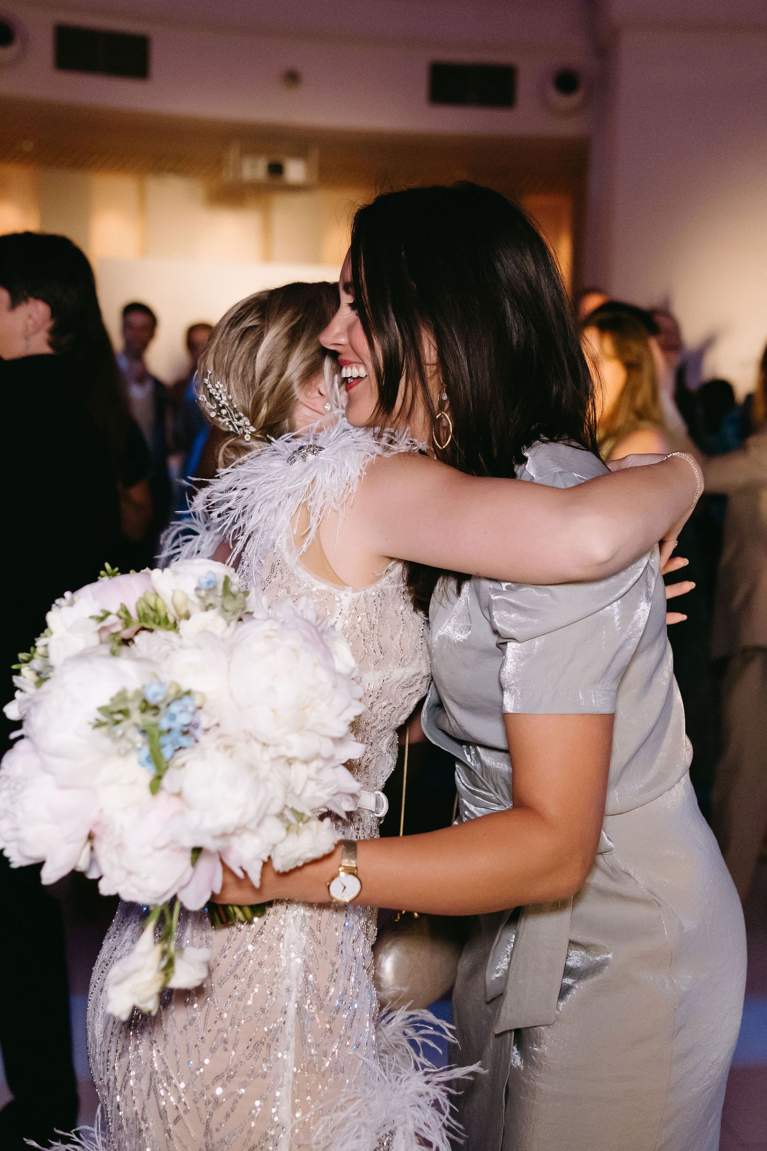 A heartfelt embrace between a bride and wedding guest holding a white bouquet.
