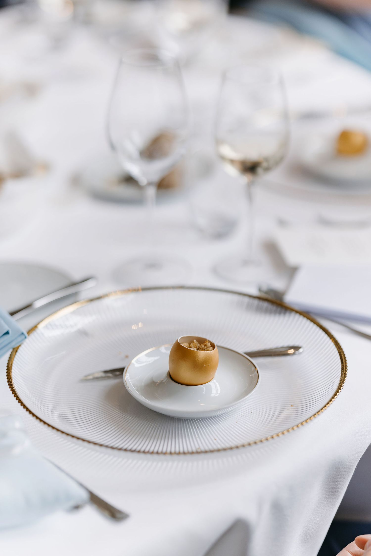 Elegant white and gold place settings with fine china plates at a formal wedding reception.