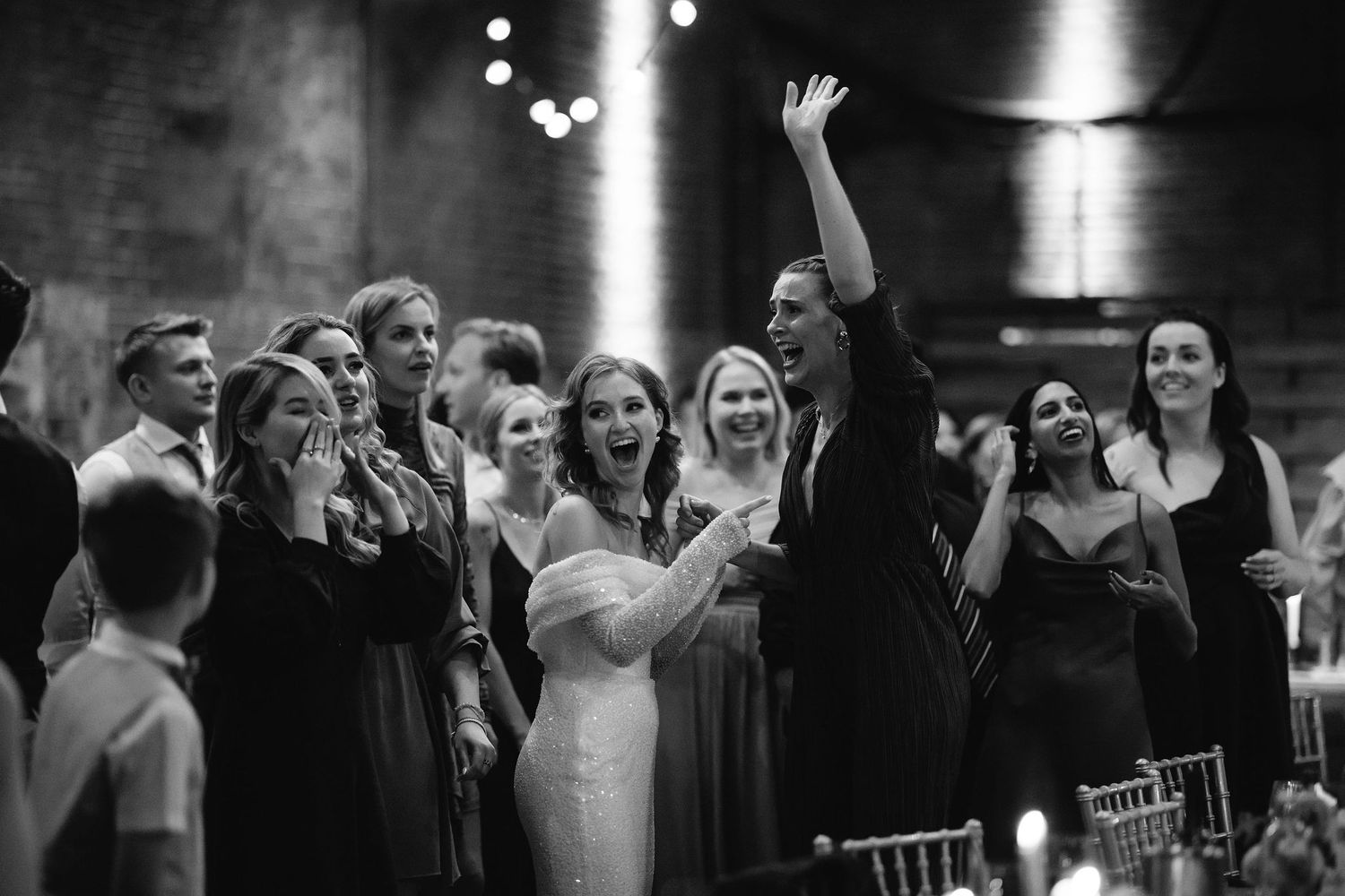 Wedding reception guests dancing and celebrating on a dimly lit dance floor.