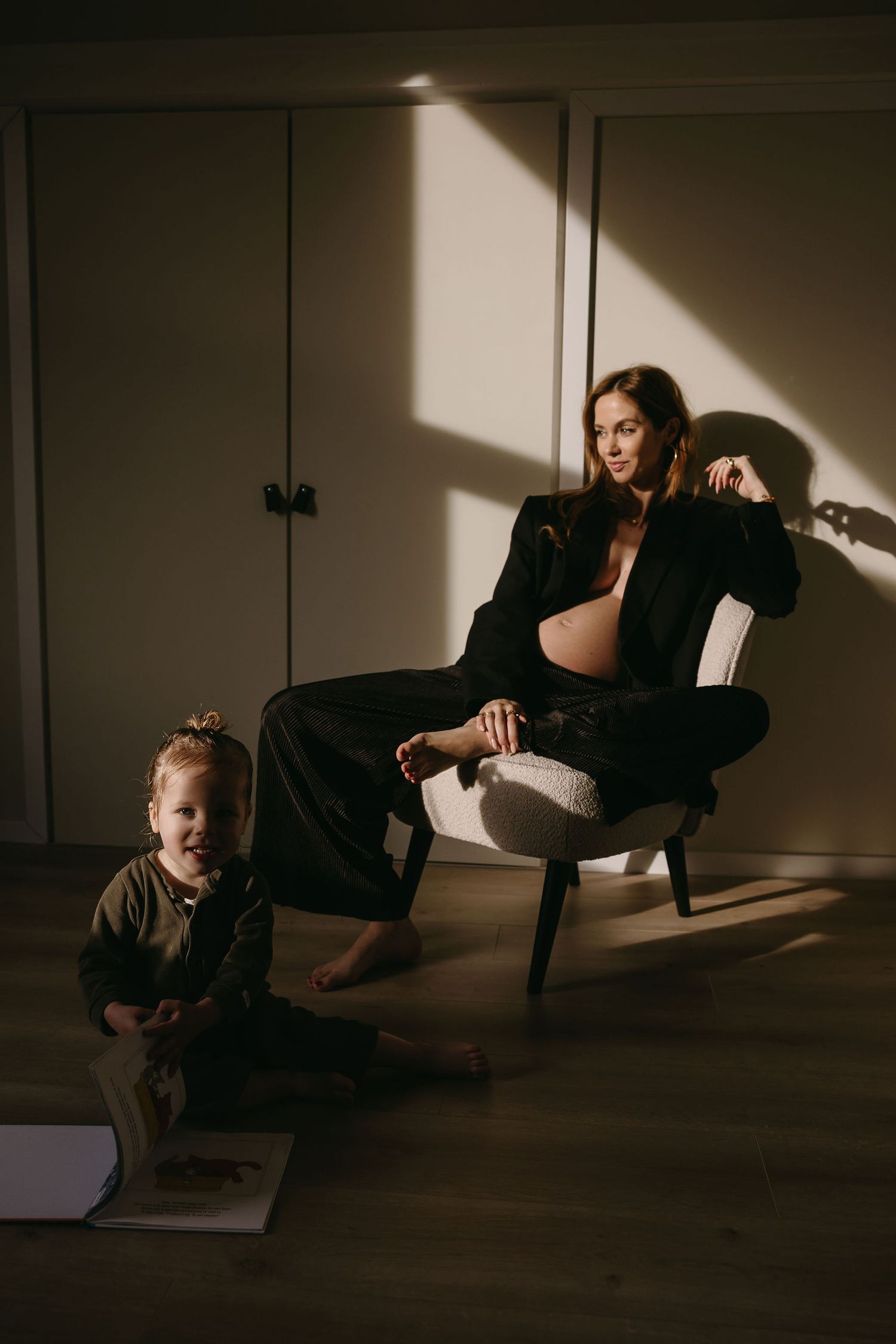 Mother and toddler share casual moment in sunlit room with dramatic shadows.