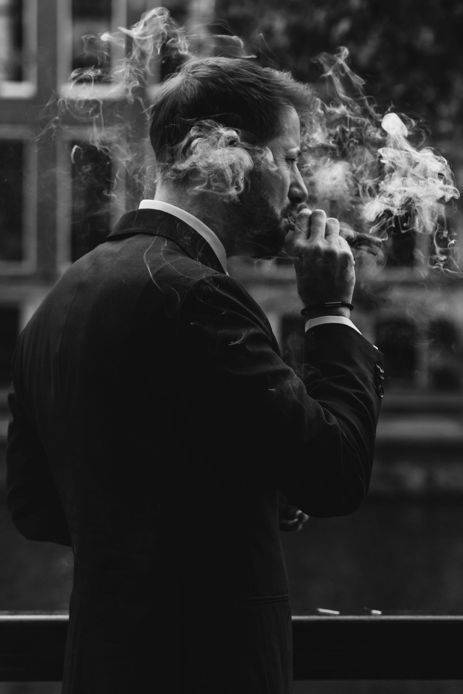 Black and white portrait of a groom in formal attire smoking with dramatic wisps of smoke.