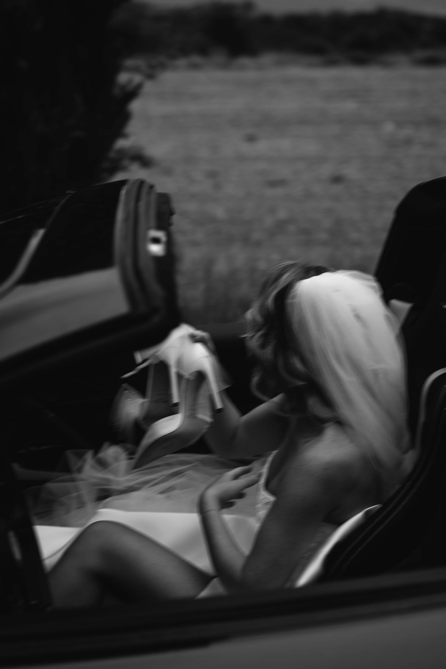 Black and white photo of a bride in a car showing elegant details of her wedding dress and veil.