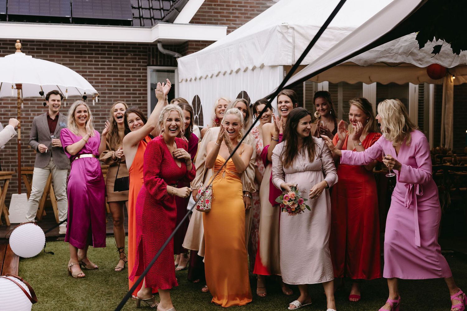 Wedding guests in vibrant dresses celebrate outdoors with balloons and champagne.
