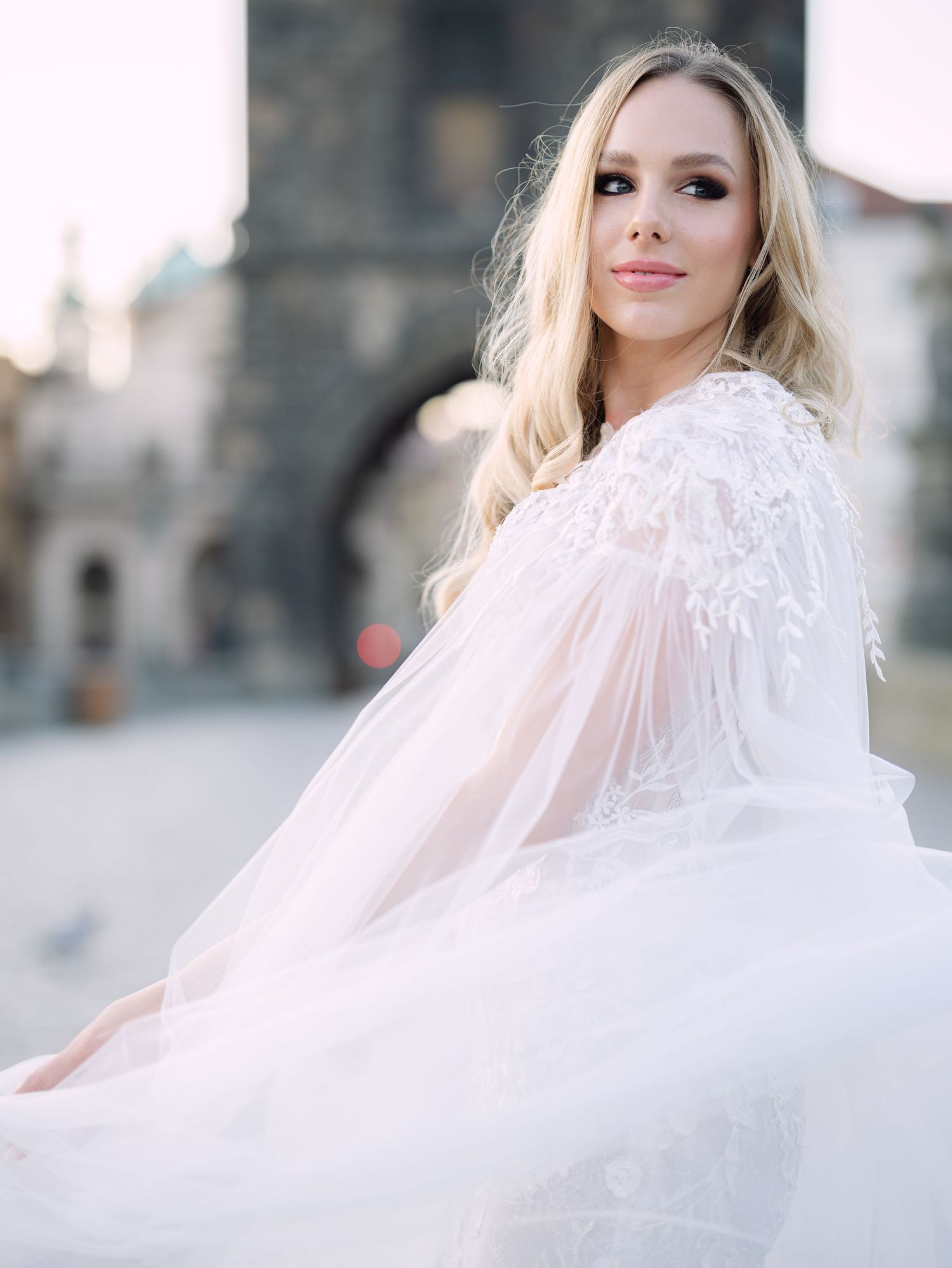 Elegant bride in a Kozarics Viktor bridal gown posing on Charles Bridge in Prague during a romantic destination elopement by Hang Pham