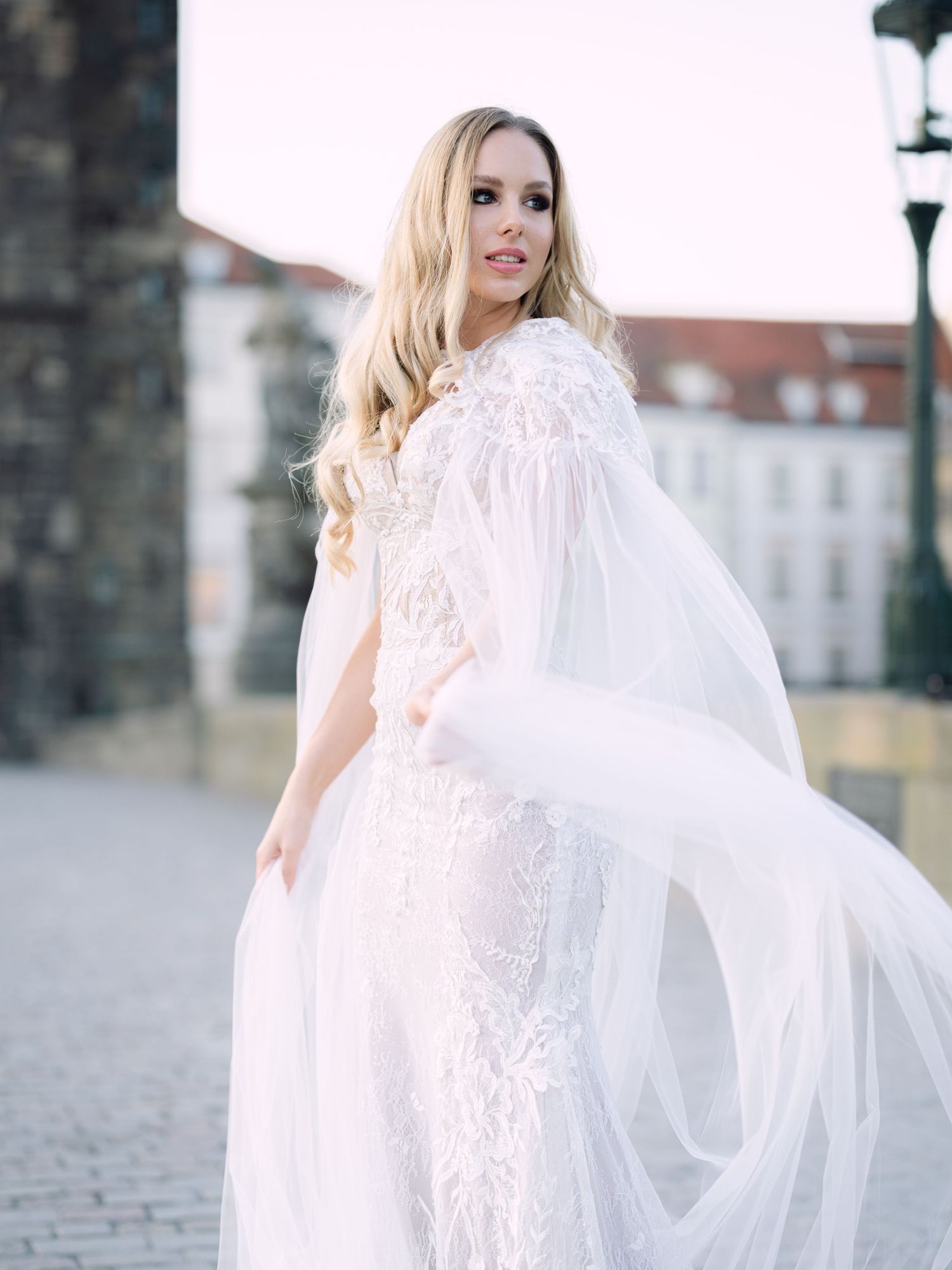 Elegant bride in a Kozarics Viktor bridal gown posing on Charles Bridge in Prague during a romantic destination elopement by Hang Pham