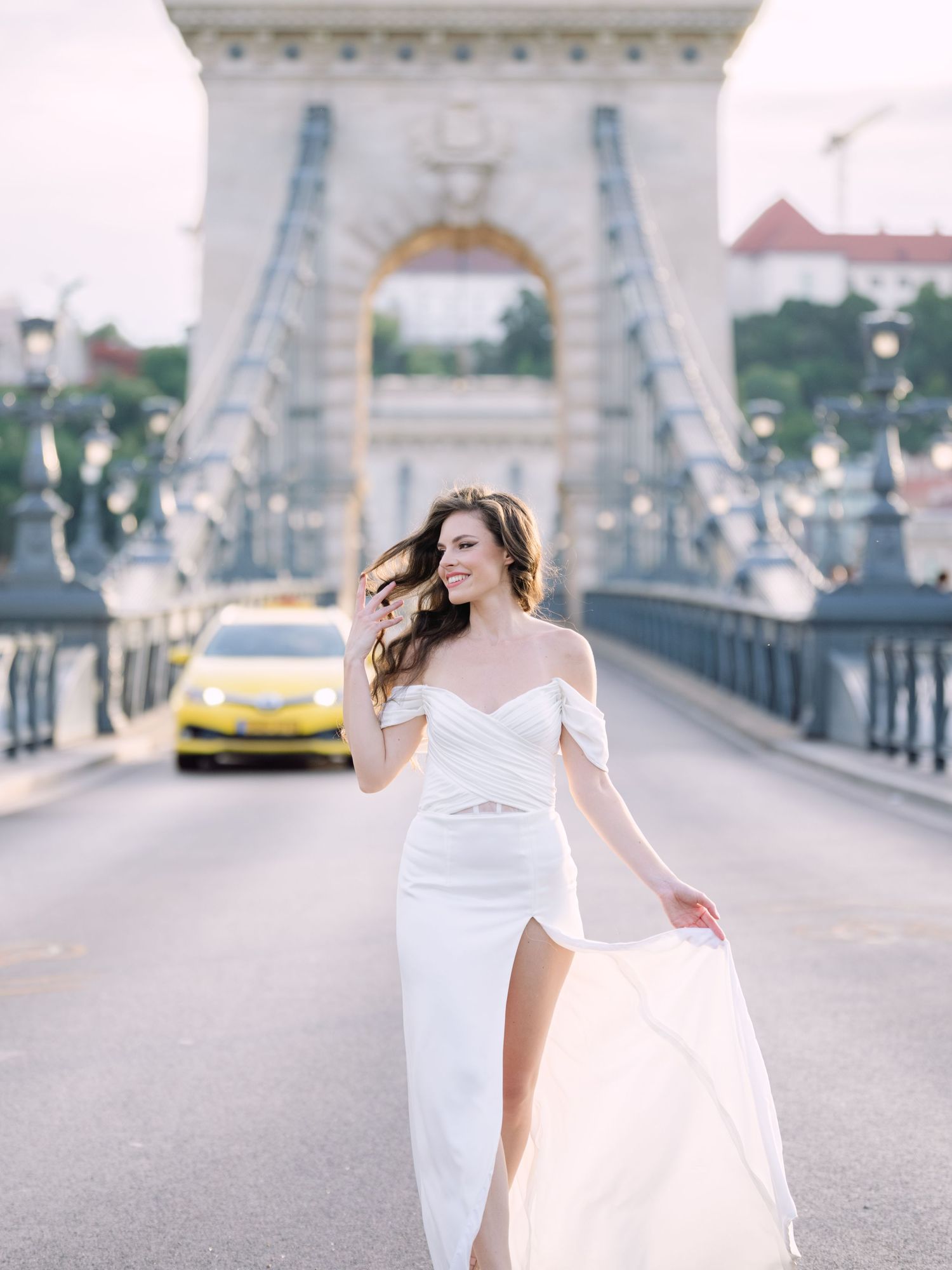 Elegant bride in a Leya Couture wedding dress posing on Budapest’s iconic Chain Bridge during a golden hour destination wedding editorial