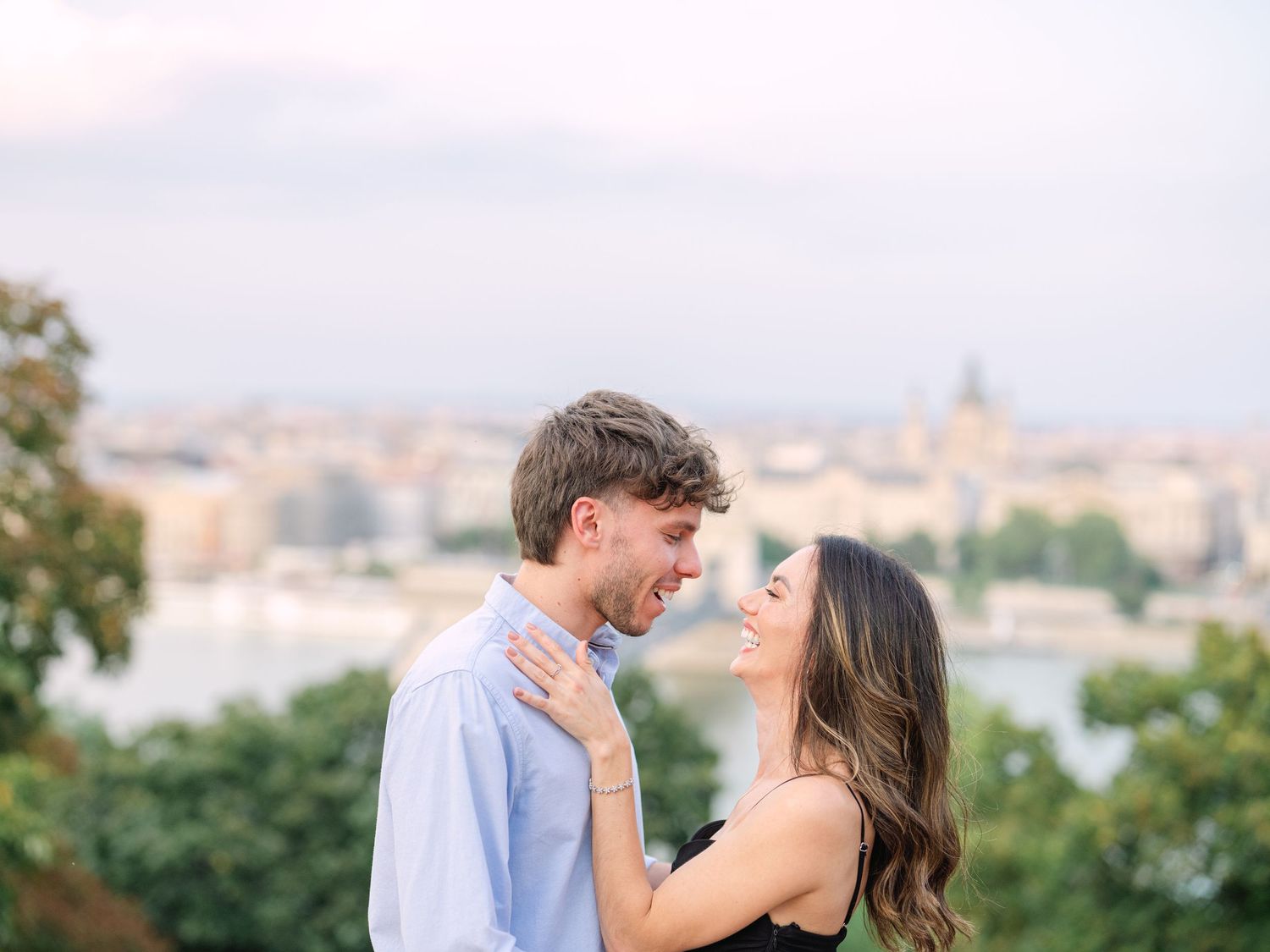 Elegant couple laughing and posing around Buda Castle in Budapest with scenic city views in the background during an couple portrait session
