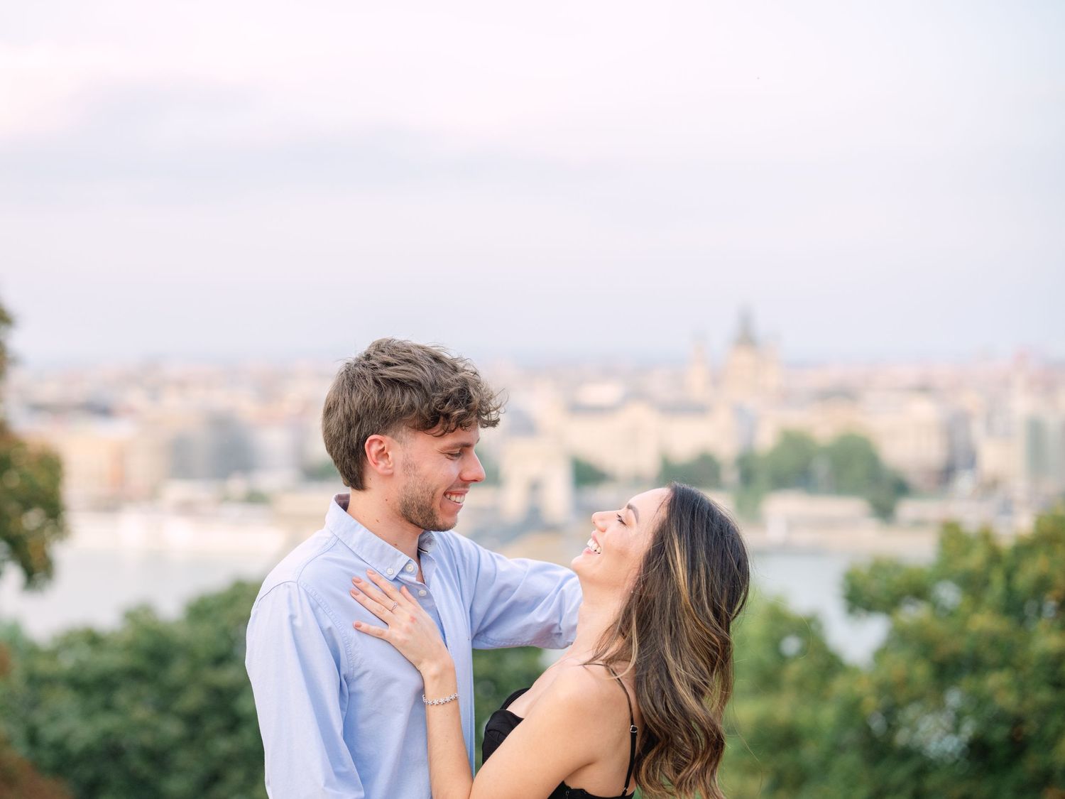 Elegant couple laughing and posing around Buda Castle in Budapest with scenic city views in the background during an couple portrait session