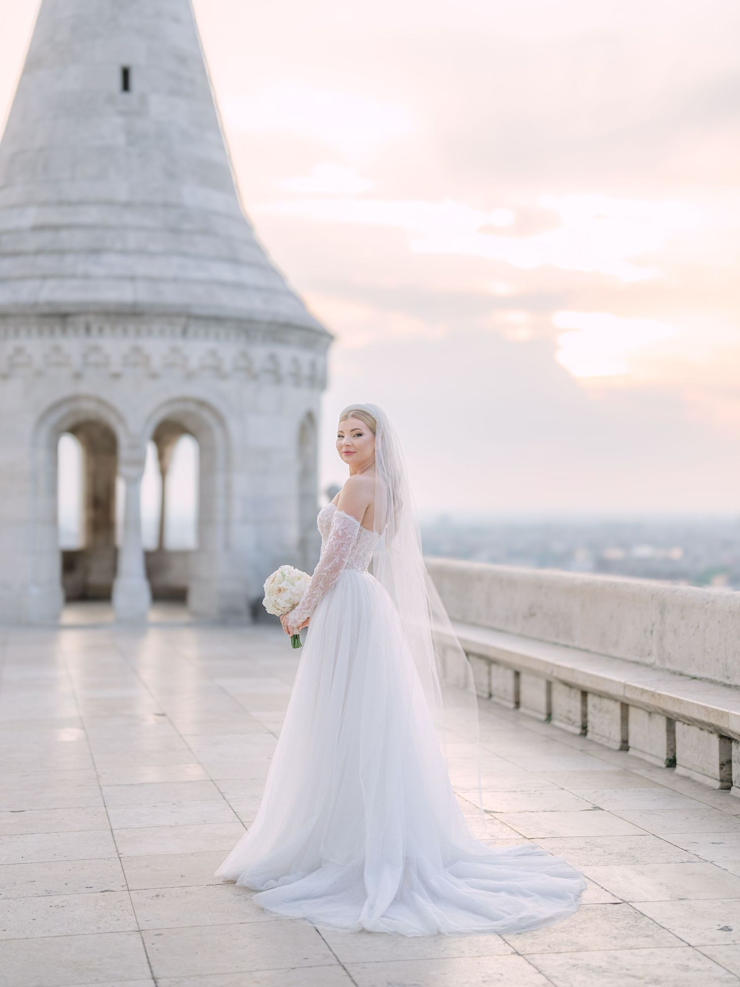 Captivating bride in a La Mariée dress posing at sunrise on Fisherman’s Bastion in Budapest during a pre-wedding session by Hang Pham