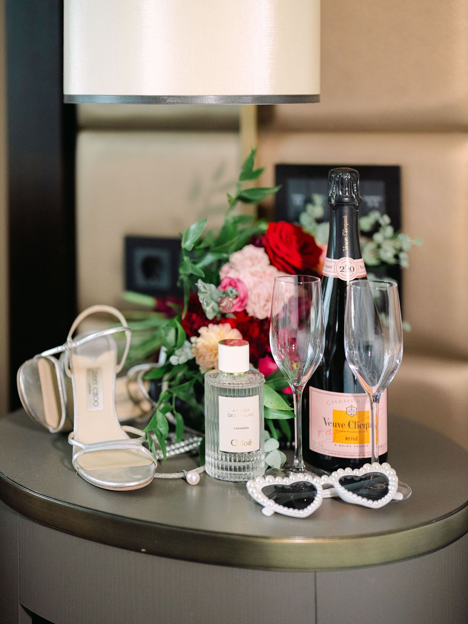 Wedding flatlay featuring Jimmy Choo bridal shoes, Tiffany rings, Chloé perfume, and champagne, styled for a luxury wedding detail shot