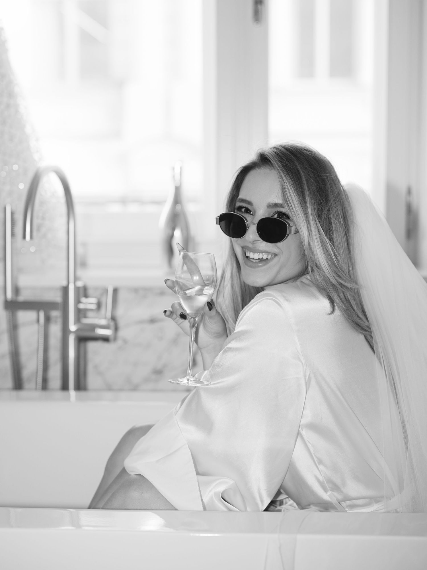 Wedding editorial at Matild Palace Budapest featuring bride with champagne and sunglasses in a luxurious bathroom, captured in a flash shot