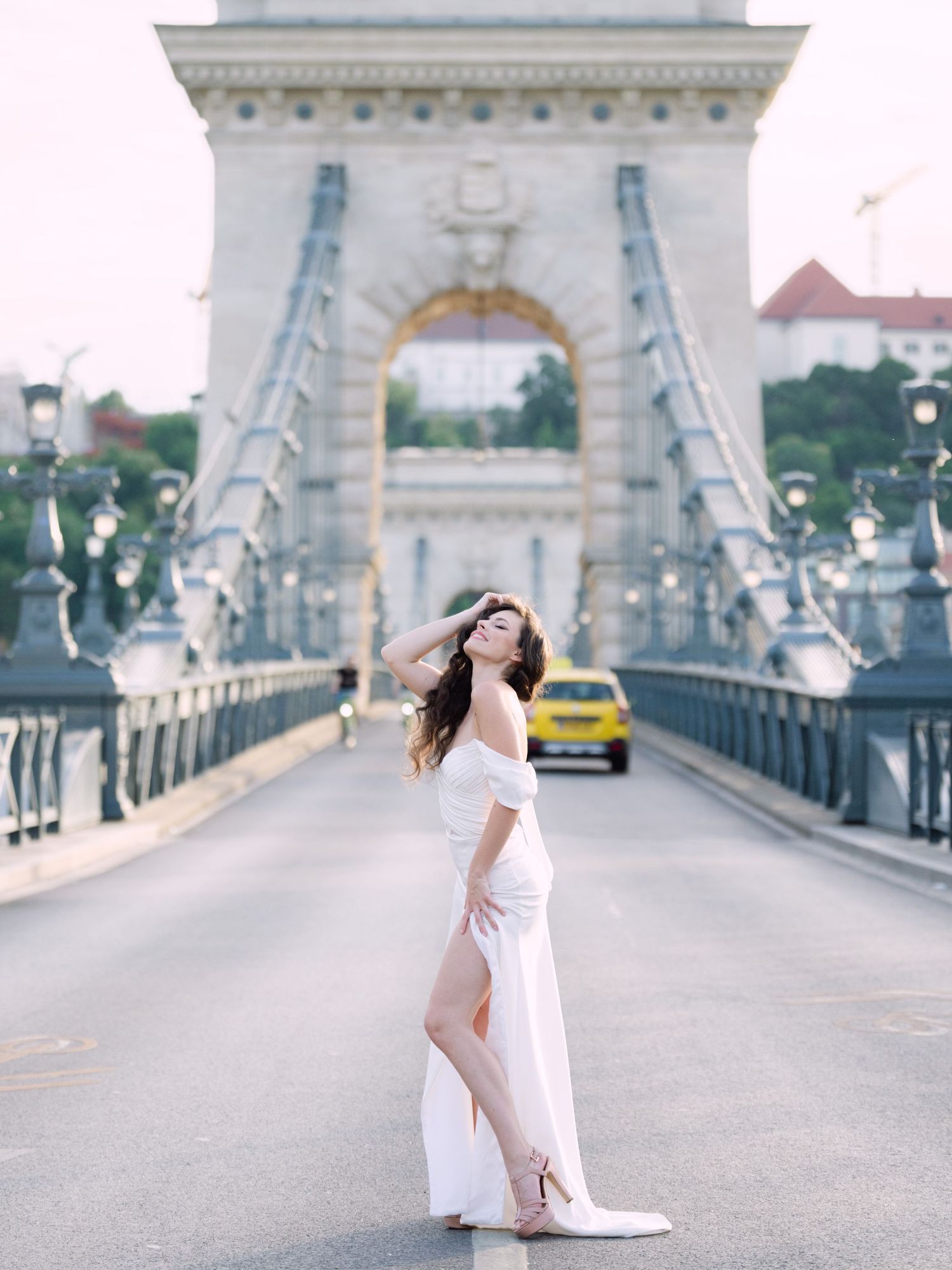 Elegant bride in a Leya Couture wedding dress posing on Budapest’s iconic Chain Bridge during a golden hour destination wedding editorial