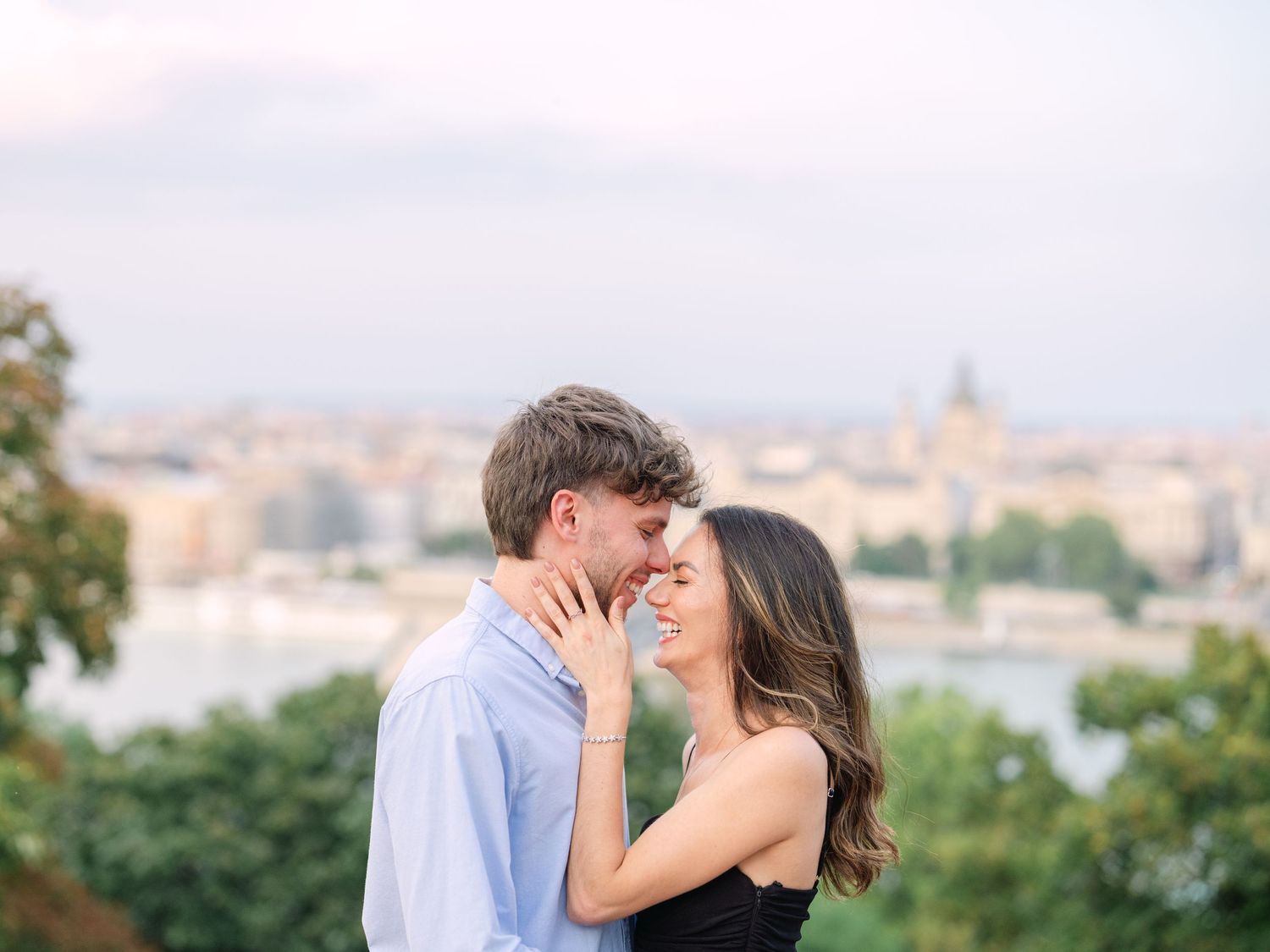 Elegant couple laughing and posing around Buda Castle in Budapest with scenic city views in the background during an couple portrait session