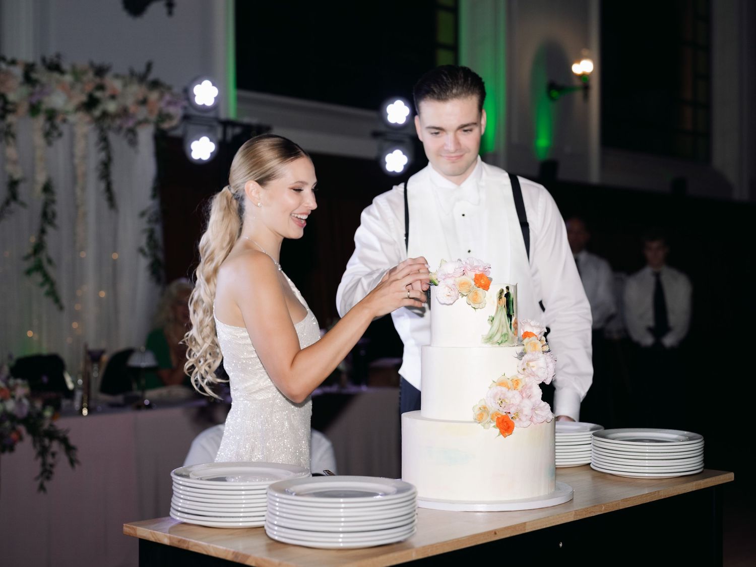 Elegant high-society couple cutting their wedding cake in the luxurious Buda Castle Royal Riding Hall, celebrating in a grand setting