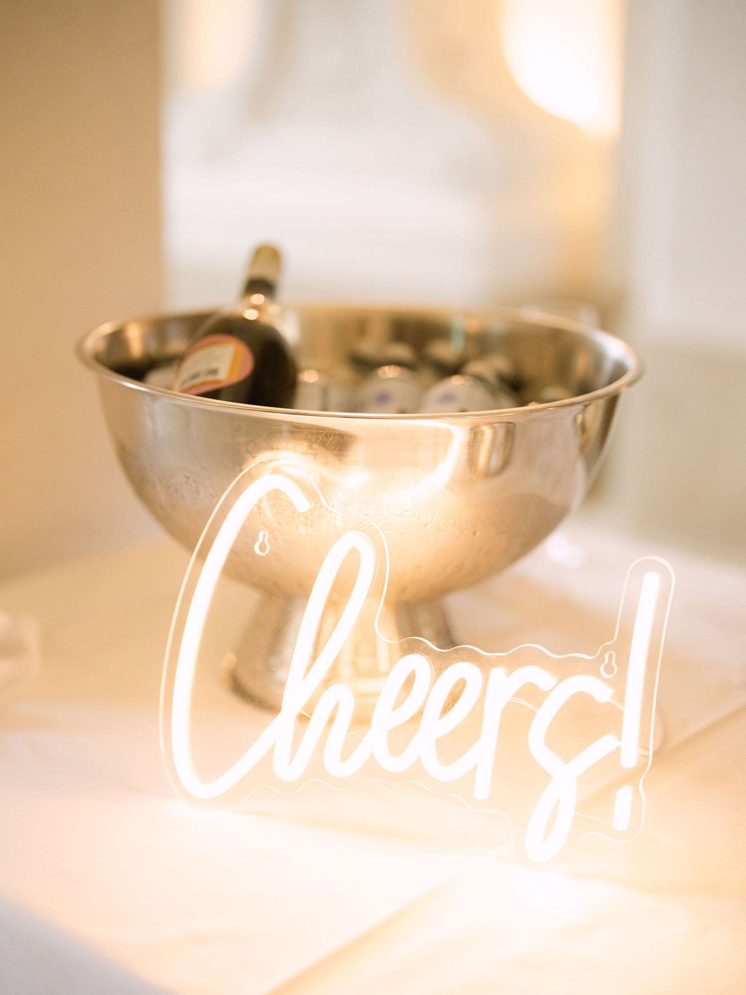 Wedding cocktail hour with stylish drinks setup and glowing 'Cheers' neon sign, creating a vibrant and celebratory atmosphere