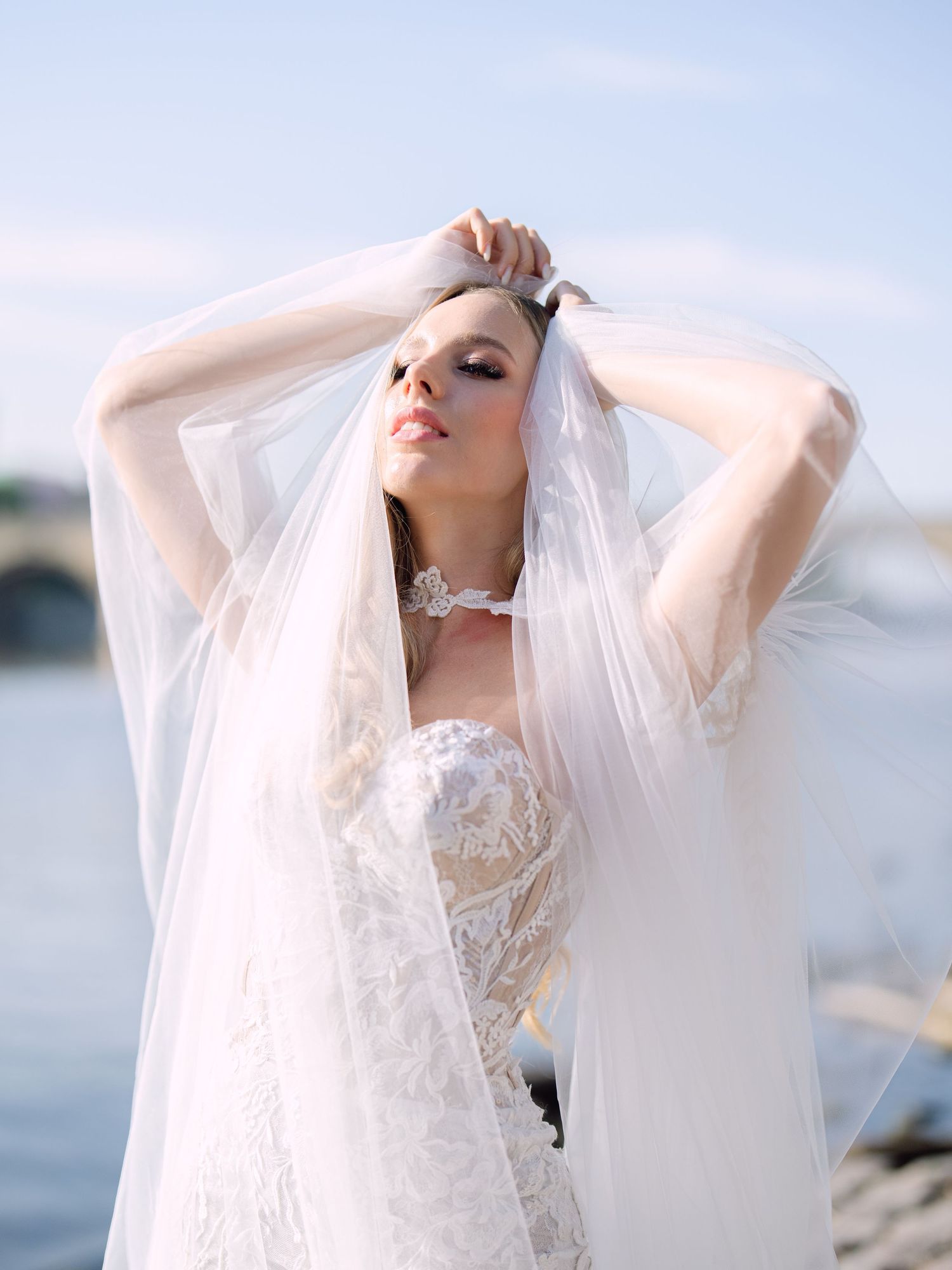 Elegant bride posing in Kozarics Viktor bridal couture by the Vltava River in Prague, captured during a destination wedding editorial shoot