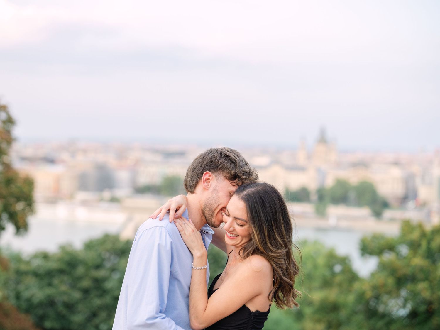 Elegant couple laughing and posing around Buda Castle in Budapest with scenic city views in the background during an couple portrait session