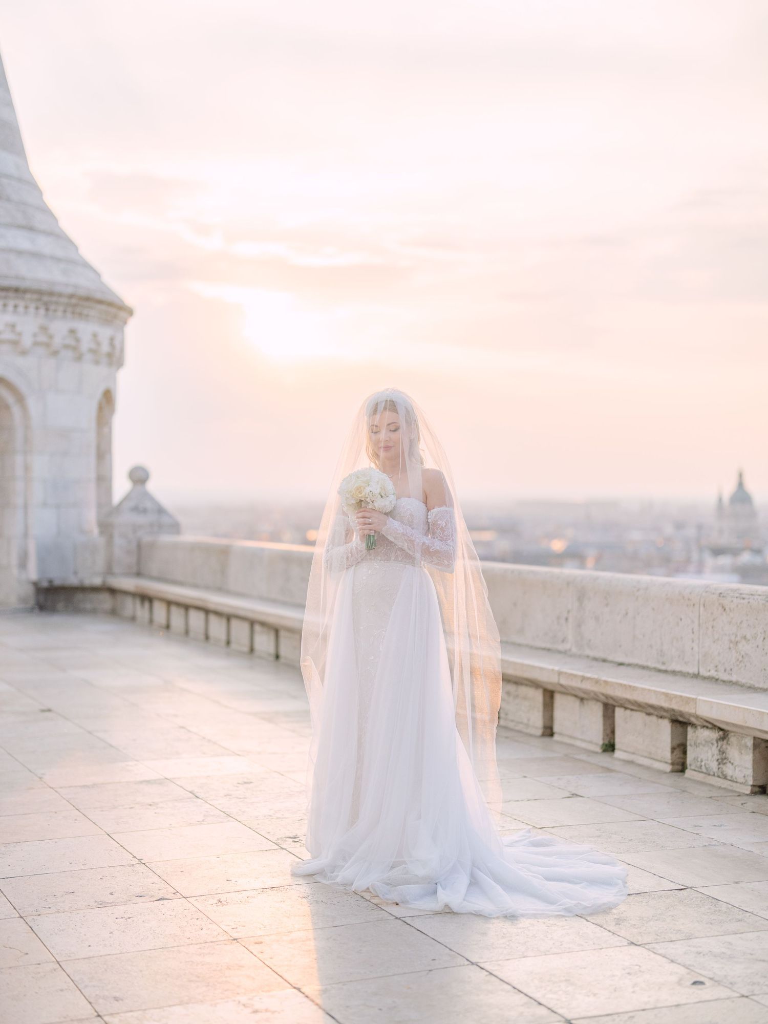 Captivating bride in a La Mariée dress posing at sunrise on Fisherman’s Bastion in Budapest during a pre-wedding session by Hang Pham
