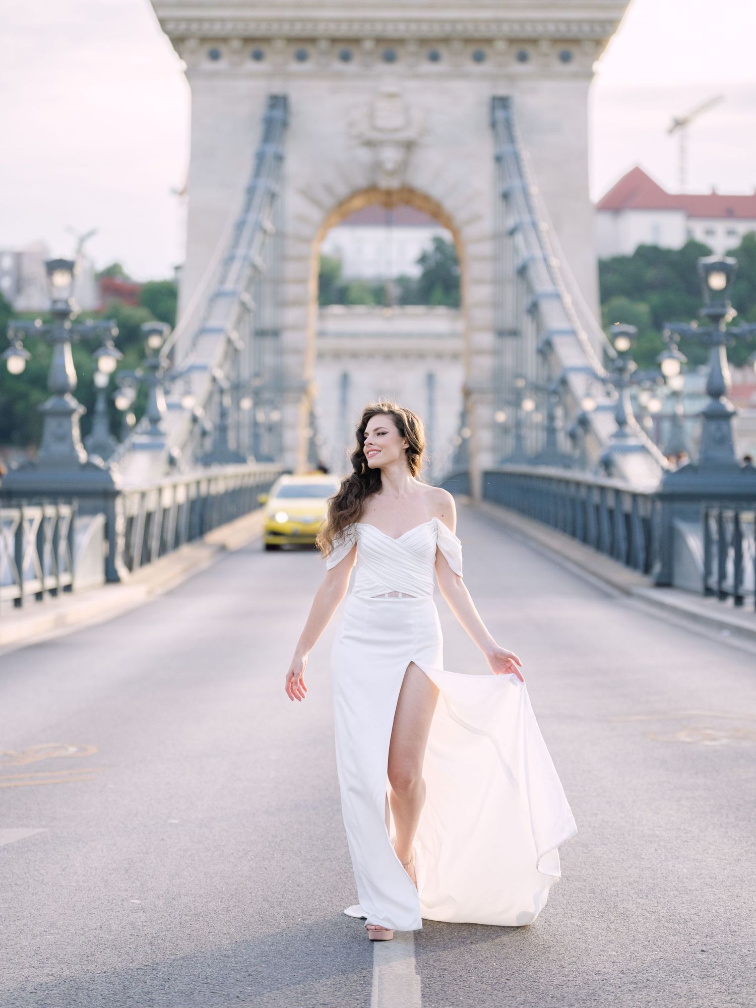 Elegant bride in a Leya Couture wedding dress posing on Budapest’s iconic Chain Bridge during a golden hour destination wedding editorial