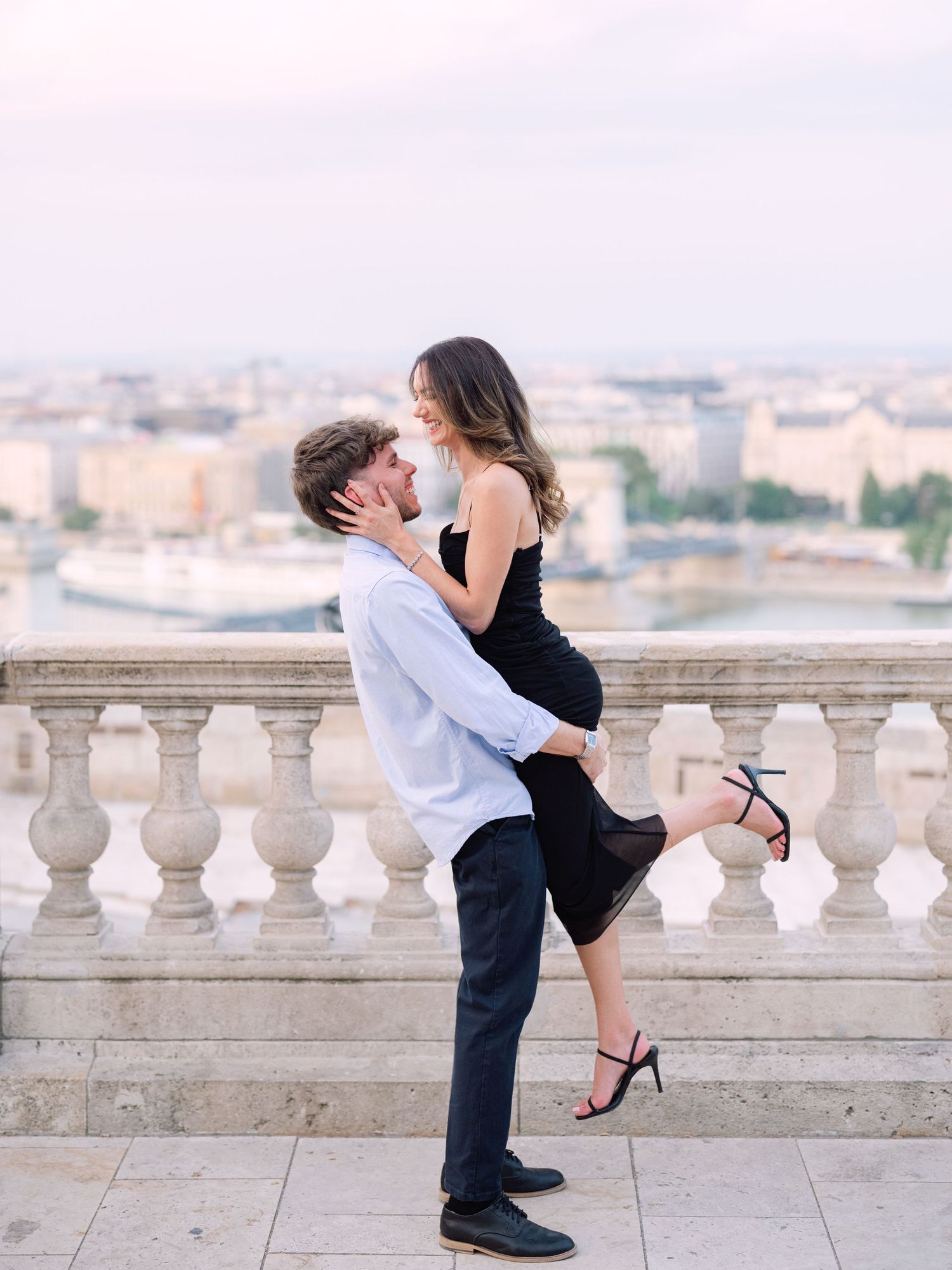 Elegant couple laughing and posing around Buda Castle in Budapest with scenic city views in the background during an couple portrait session