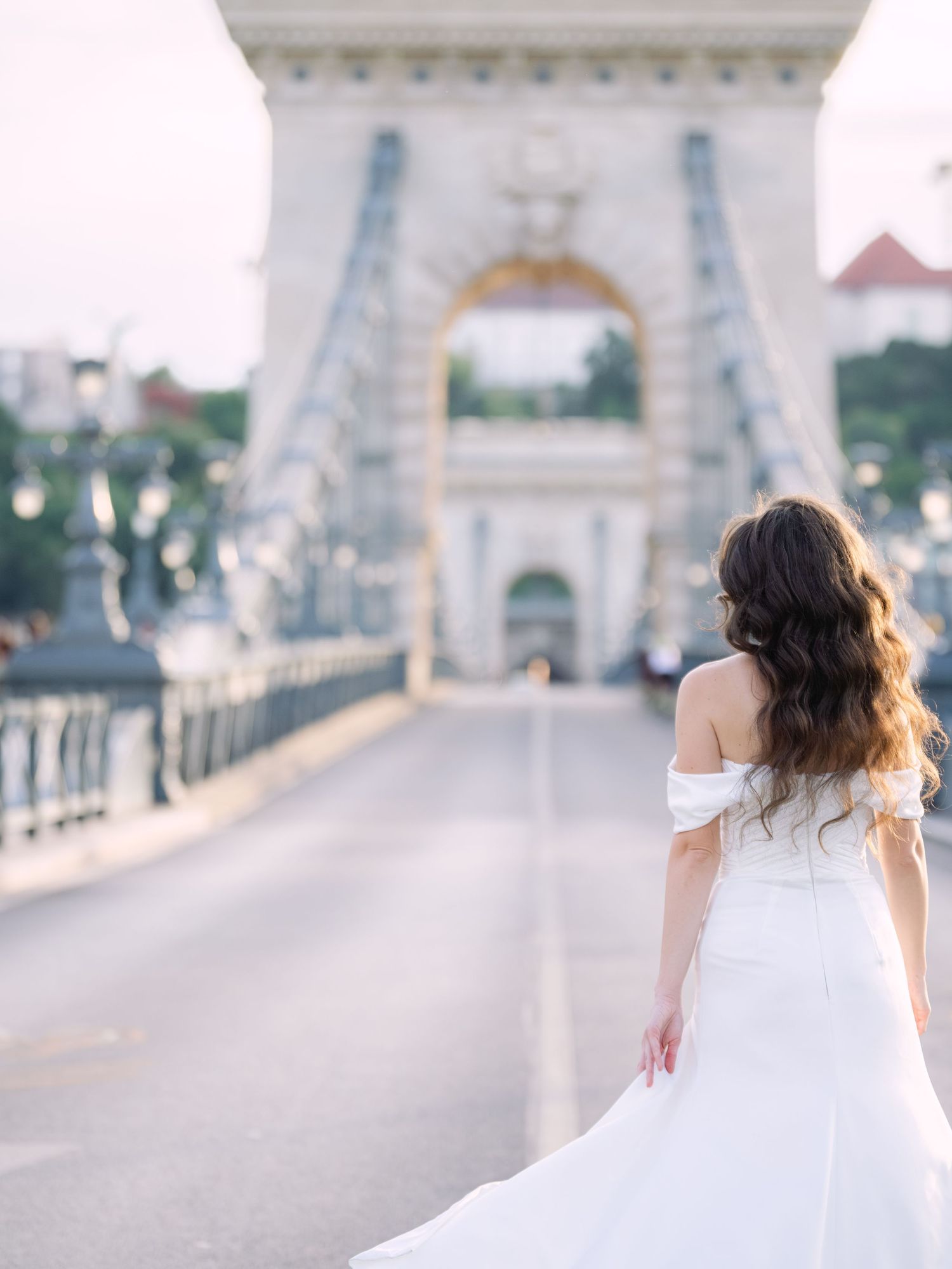 Elegant bride in a Leya Couture wedding dress posing on Budapest’s iconic Chain Bridge during a golden hour destination wedding editorial, c