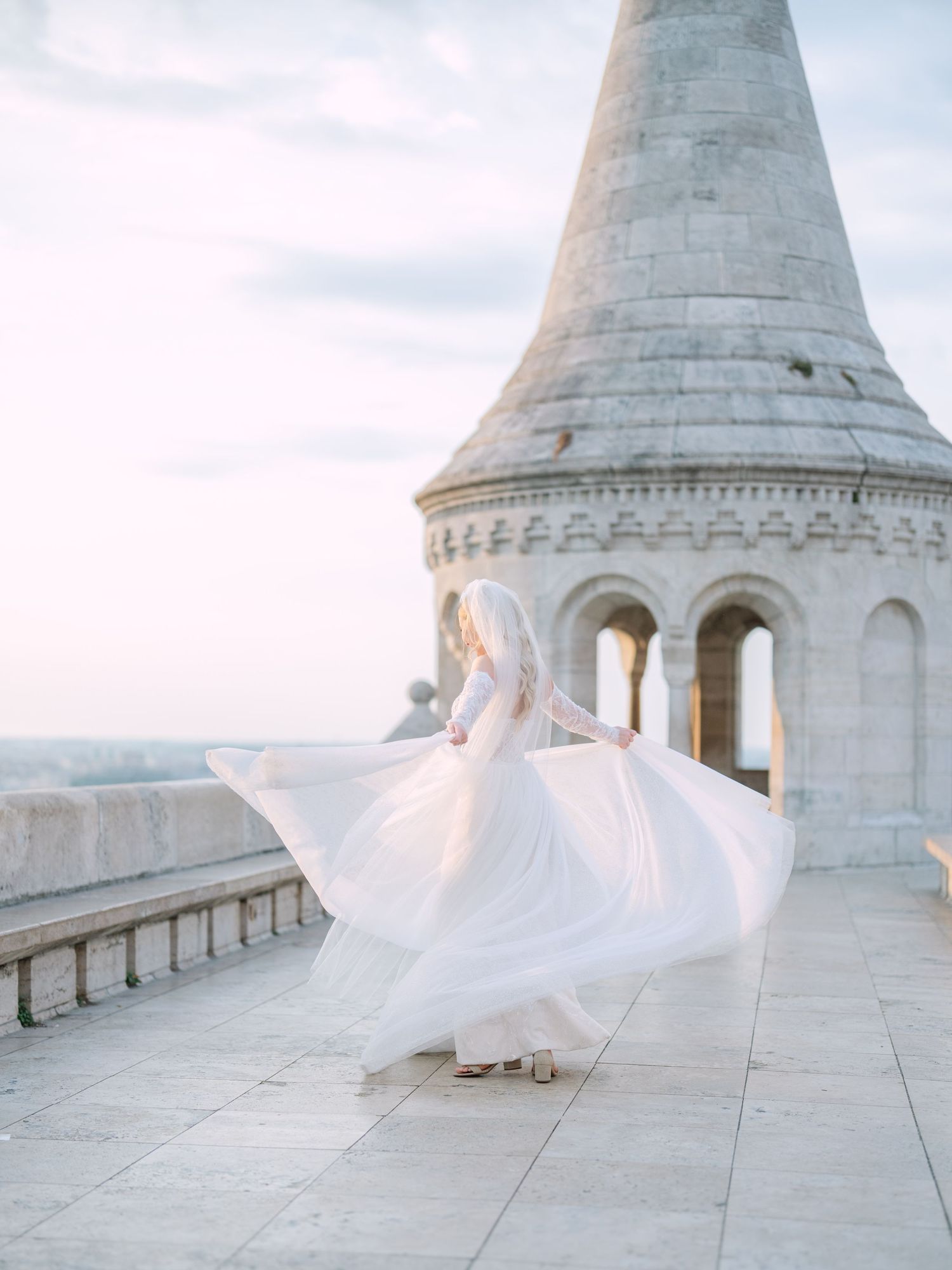 Captivating bride in a La Mariée dress posing at sunrise on Fisherman’s Bastion in Budapest during a pre-wedding session by Hang Pham