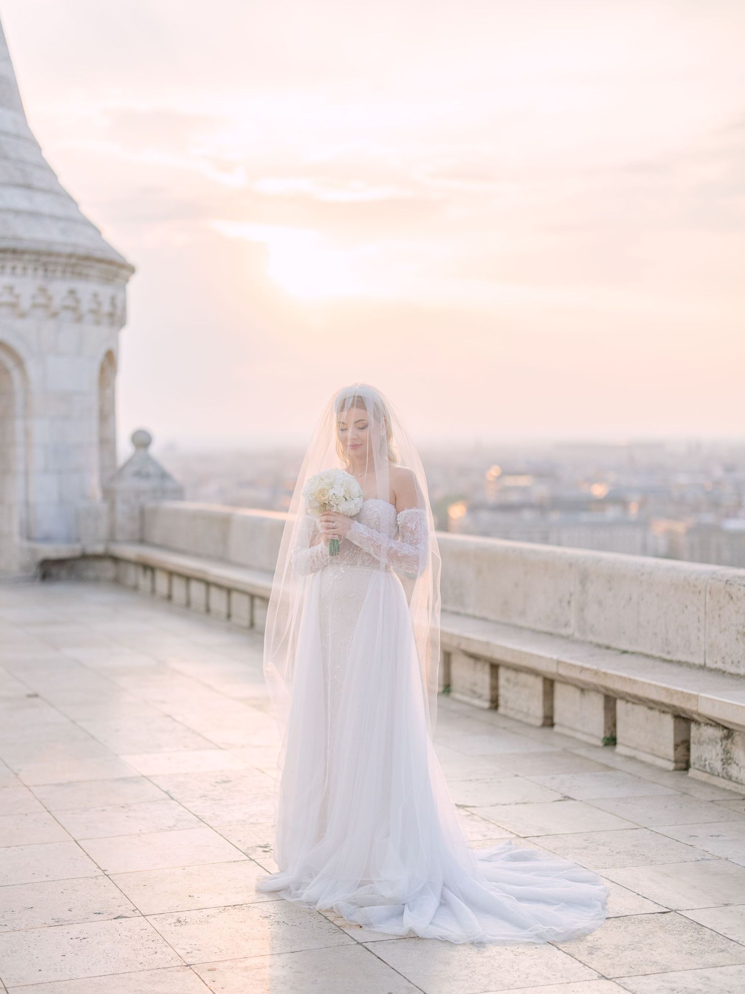 Captivating bride in a La Mariée dress posing at sunrise on Fisherman’s Bastion in Budapest during a pre-wedding session by Hang Pham
