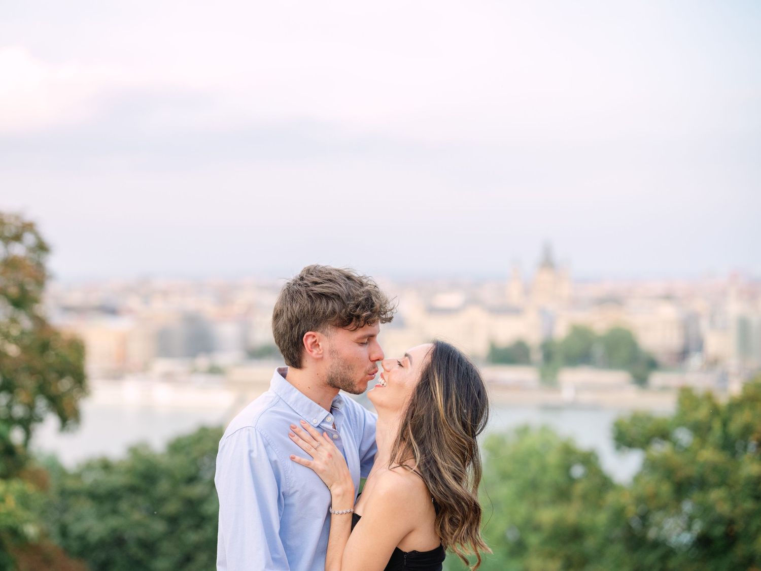 Elegant couple laughing and posing around Buda Castle in Budapest with scenic city views in the background during an couple portrait session