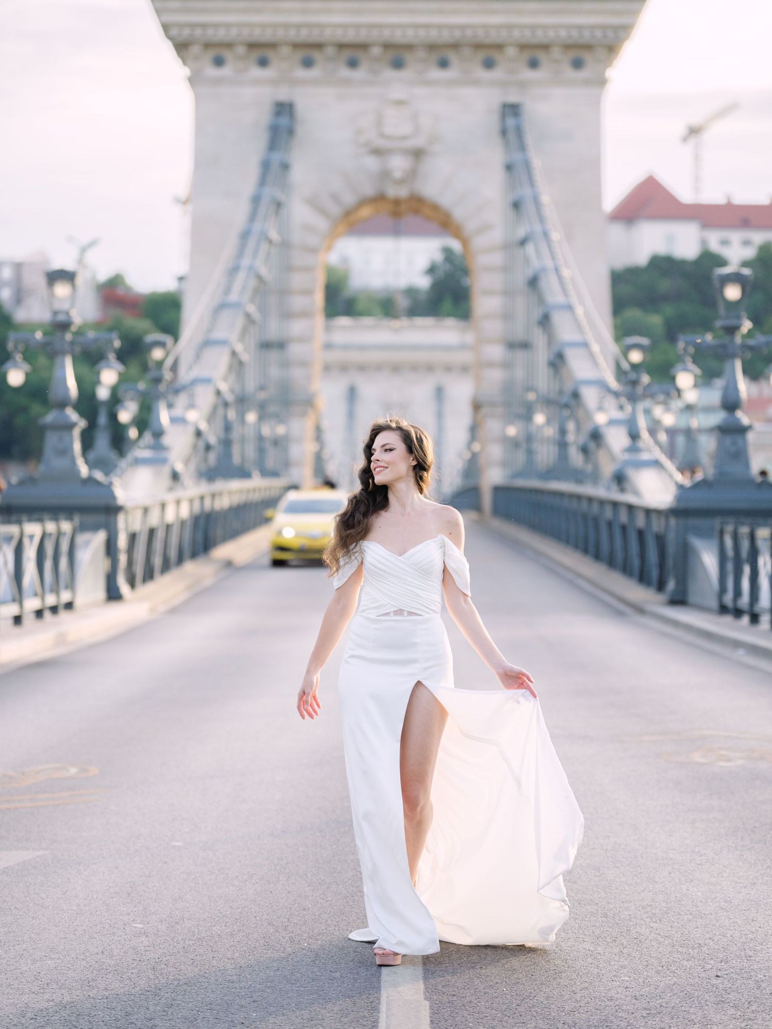 Elegant bride in a Leya Couture wedding dress posing on Budapest’s iconic Chain Bridge during a golden hour destination wedding editorial