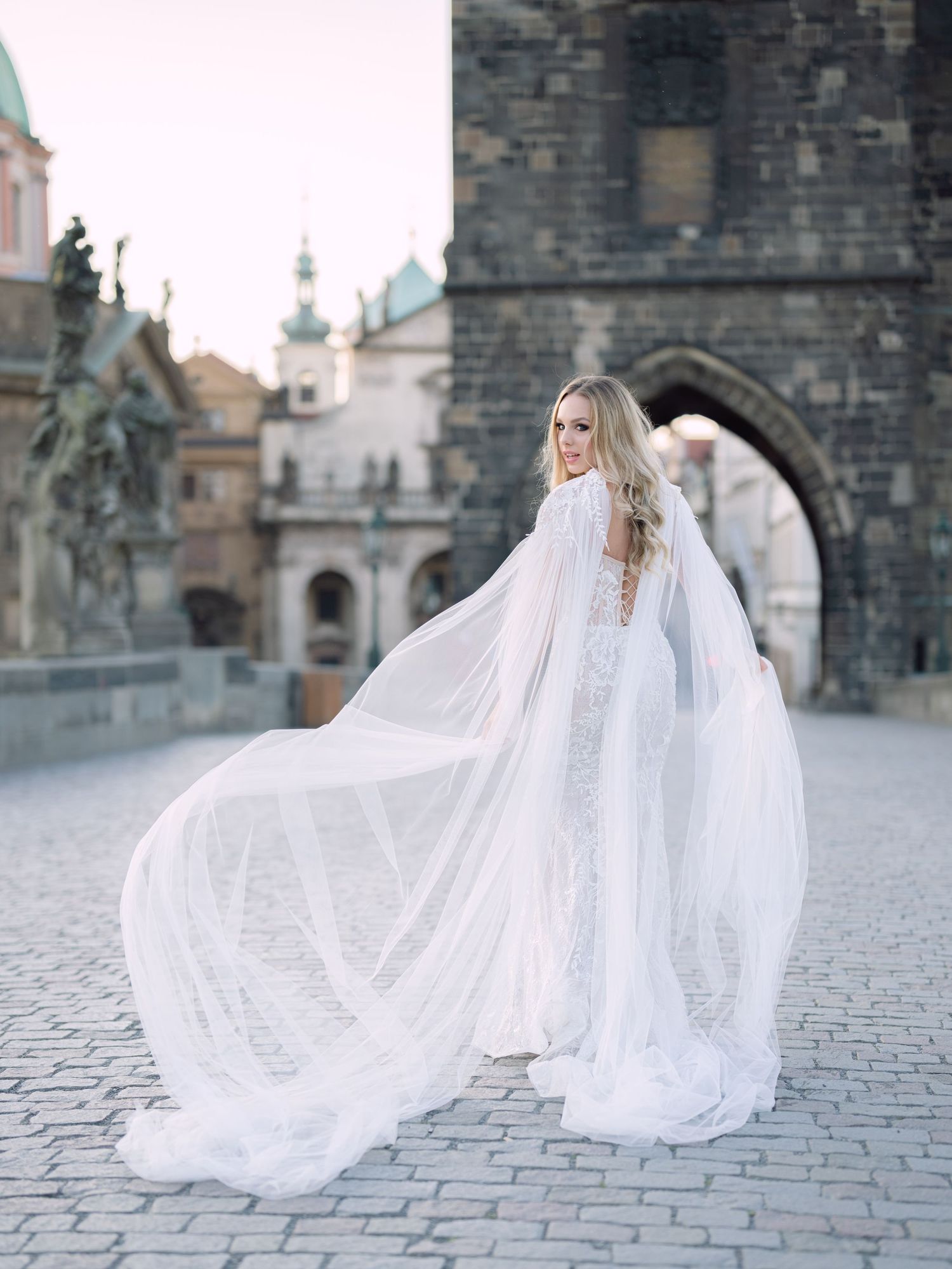 Elegant bride in a Kozarics Viktor bridal gown posing on Charles Bridge in Prague during a romantic destination elopement by Hang Pham