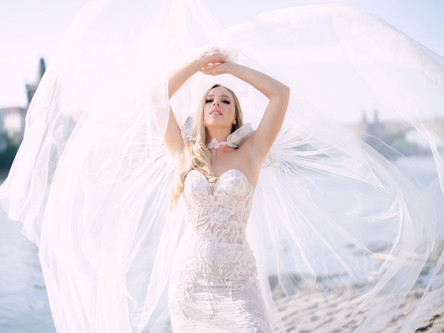 Elegant bride posing in Kozarics Viktor bridal couture by the Vltava River in Prague, captured during a destination wedding editorial shoot