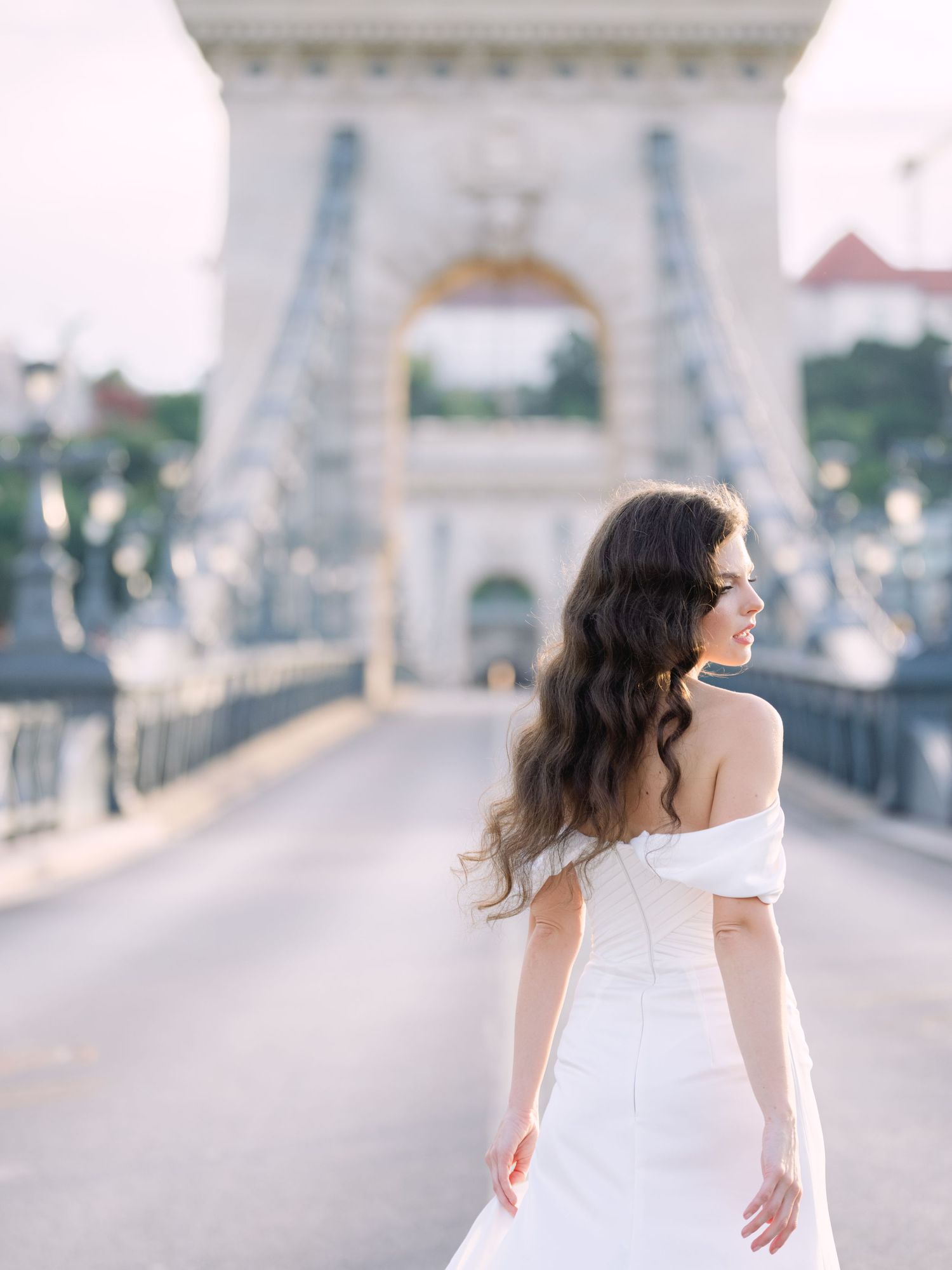 Elegant bride in a Leya Couture wedding dress posing on Budapest’s iconic Chain Bridge during a golden hour destination wedding editorial