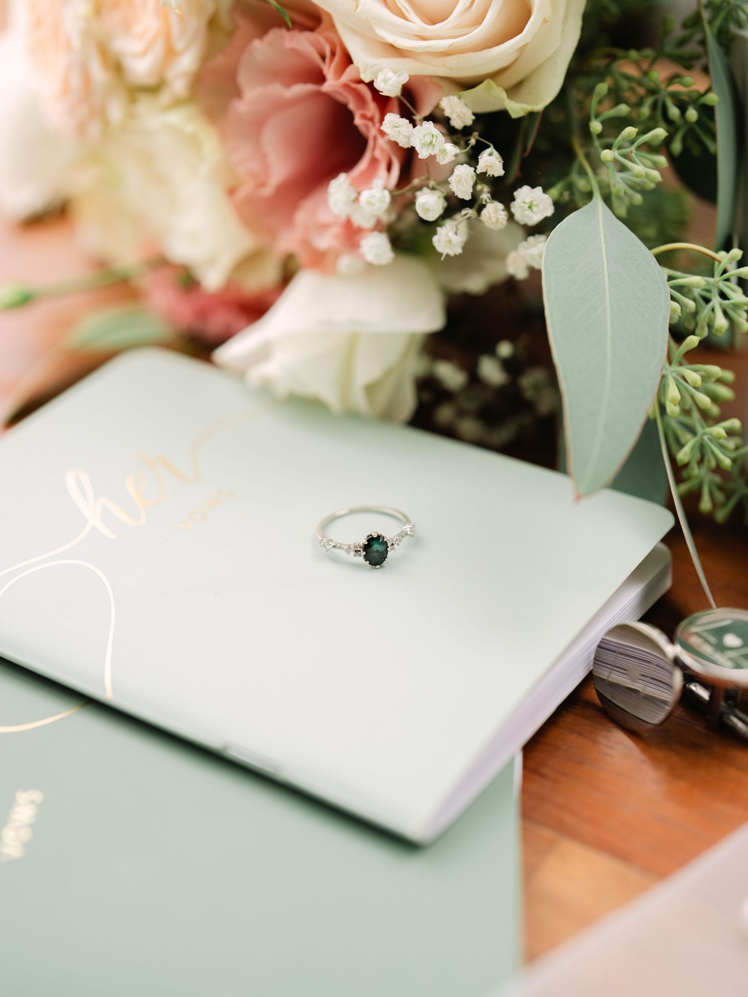Wedding flatlay featuring elegant vows suite, engagement rings, and bridal bouquet, styled for a sophisticated luxury wedding detail shot