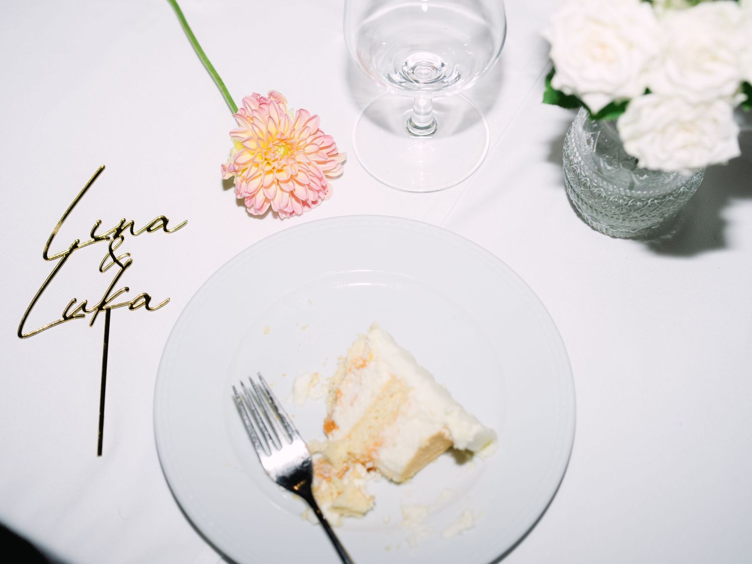 Wedding flatlay featuring the couple’s nametag, vibrant flowers, and a partially eaten cake, styled for a playful modern luxury wedding