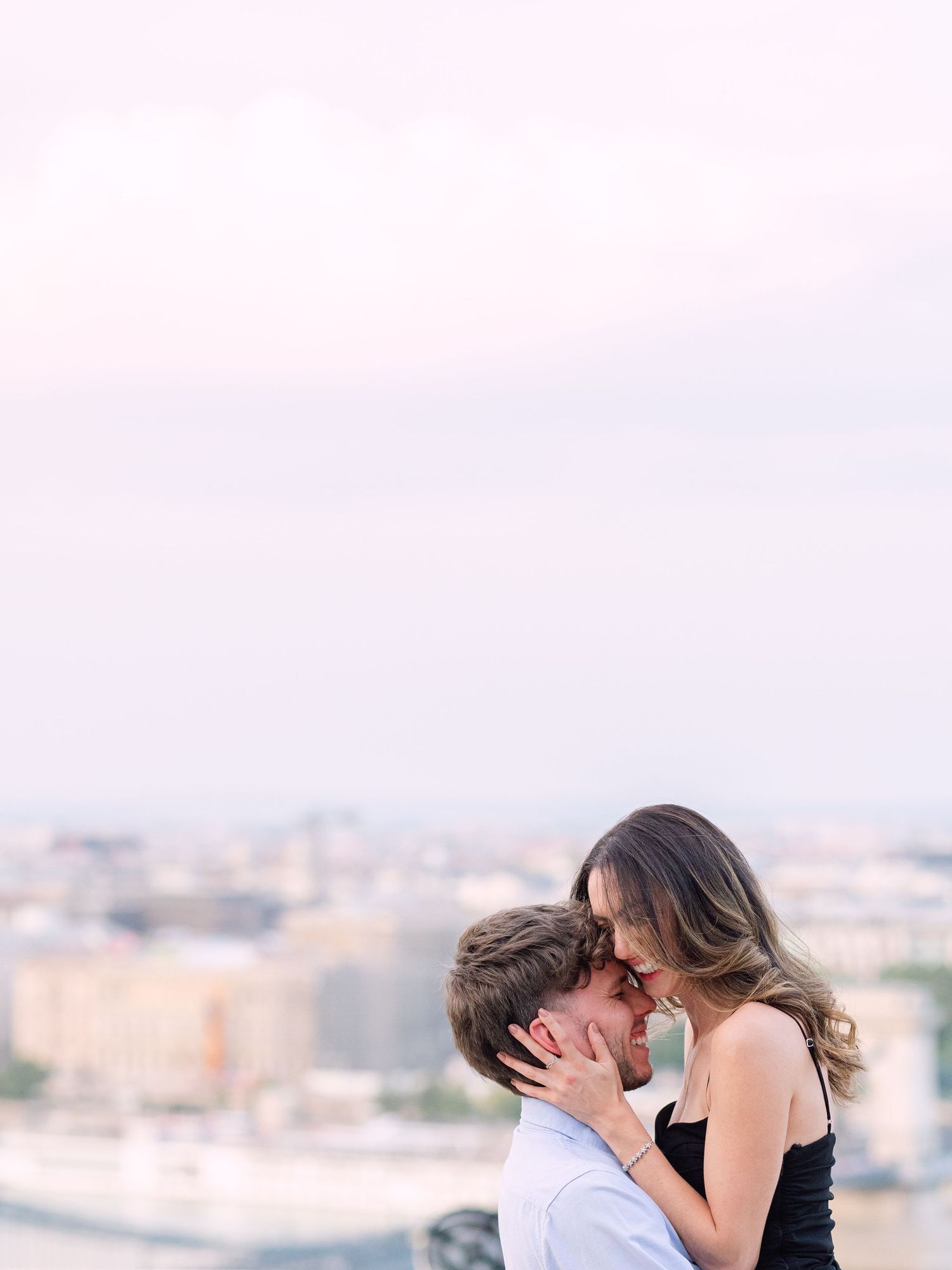 Elegant couple laughing and posing around Buda Castle in Budapest with scenic city views in the background during an couple portrait session