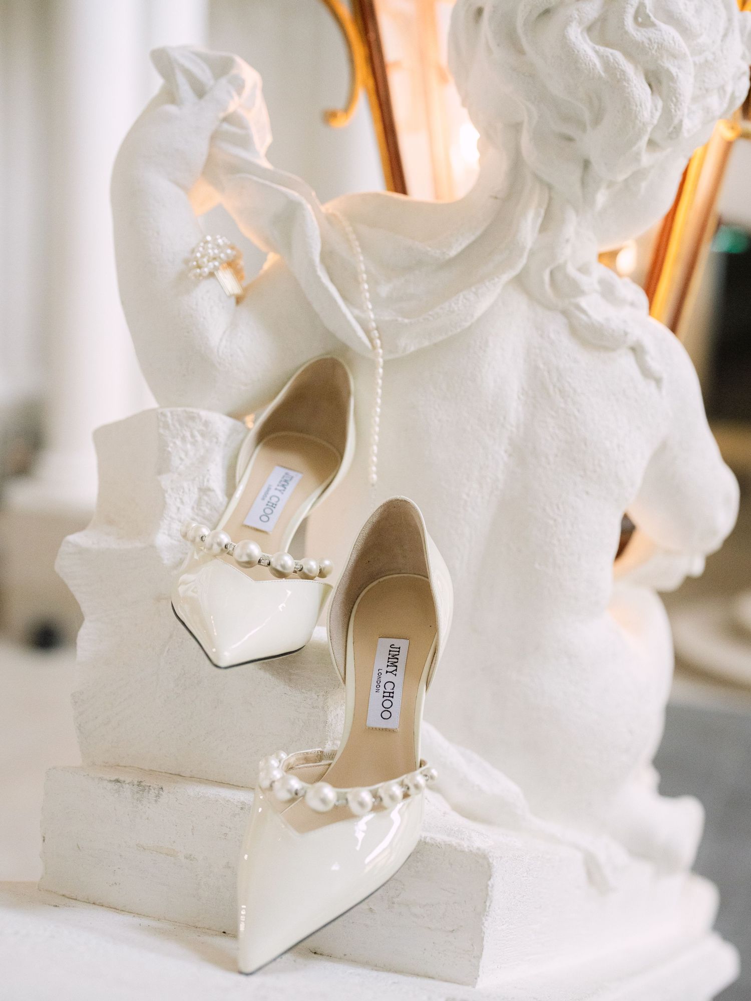 Wedding flatlay featuring elegant Jimmy Choo bridal shoes styled on an angelic statue within a luxurious Austrian castle for a timeless look