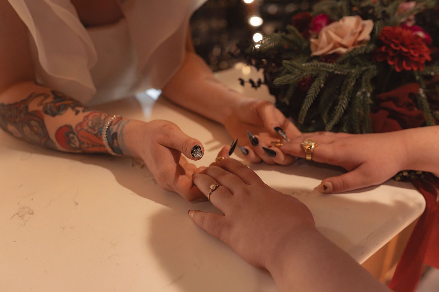 Close-up of two brides exchanging rings during wedding ceremony, one with floral tattoos.