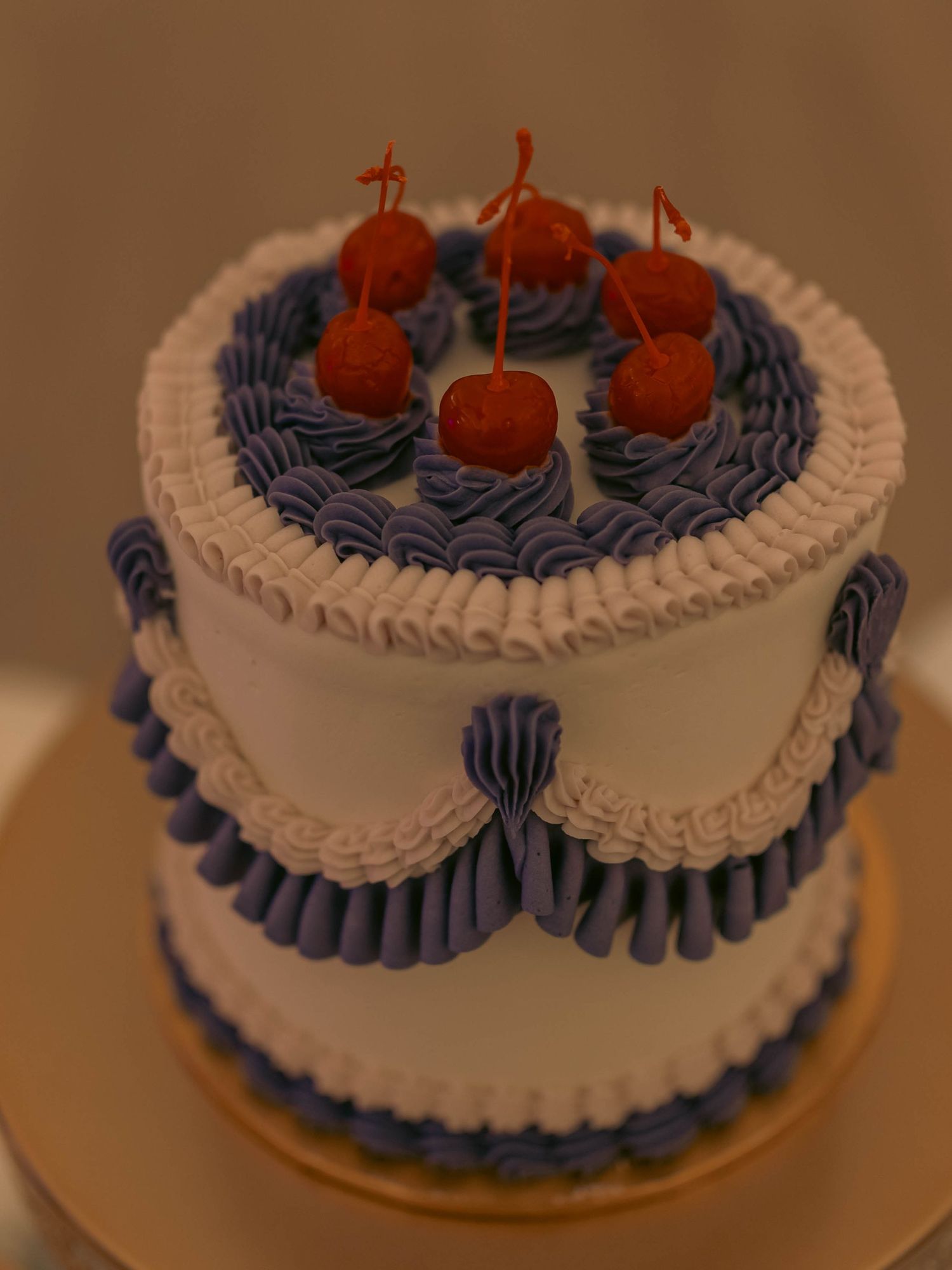 Elegant two-tier white cake with blue frosting details and four red cherries on top.