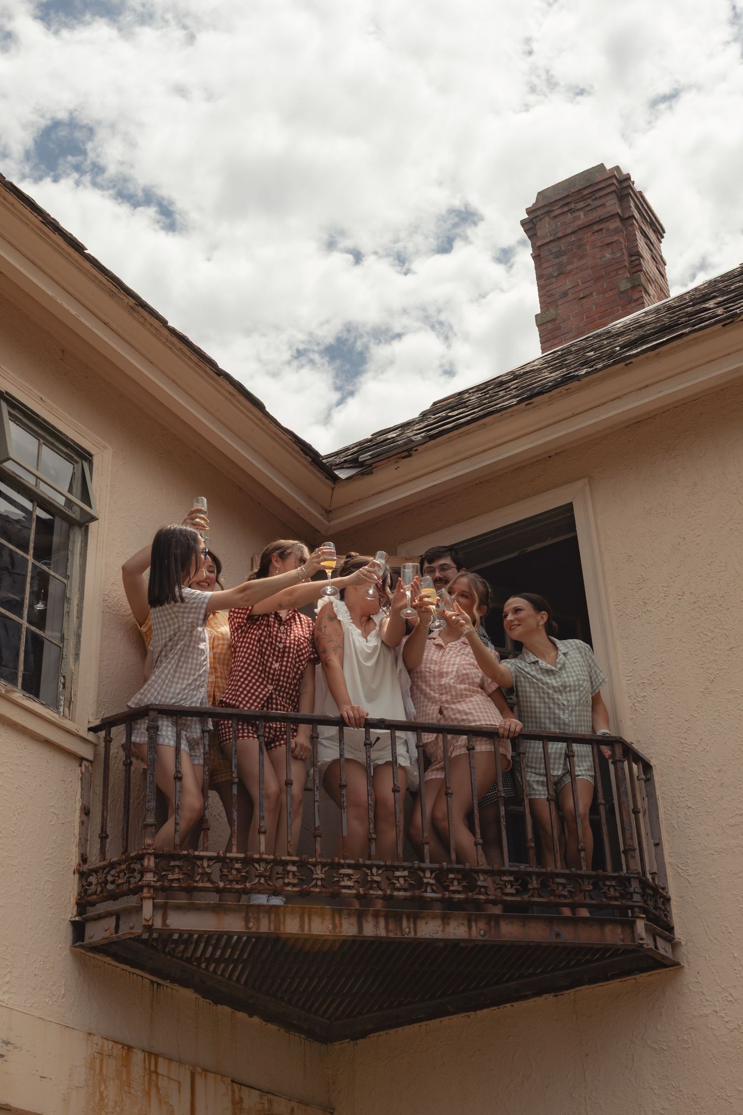 Friends toasting with champagne glasses on a rustic balcony under a cloudy sky at an outdoor celebration.
