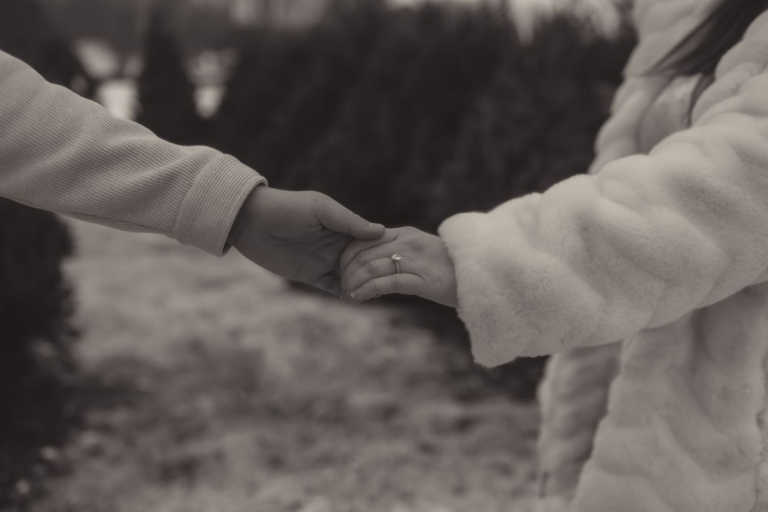 Black and white photo of a couple holding hands outdoors wearing white coats.