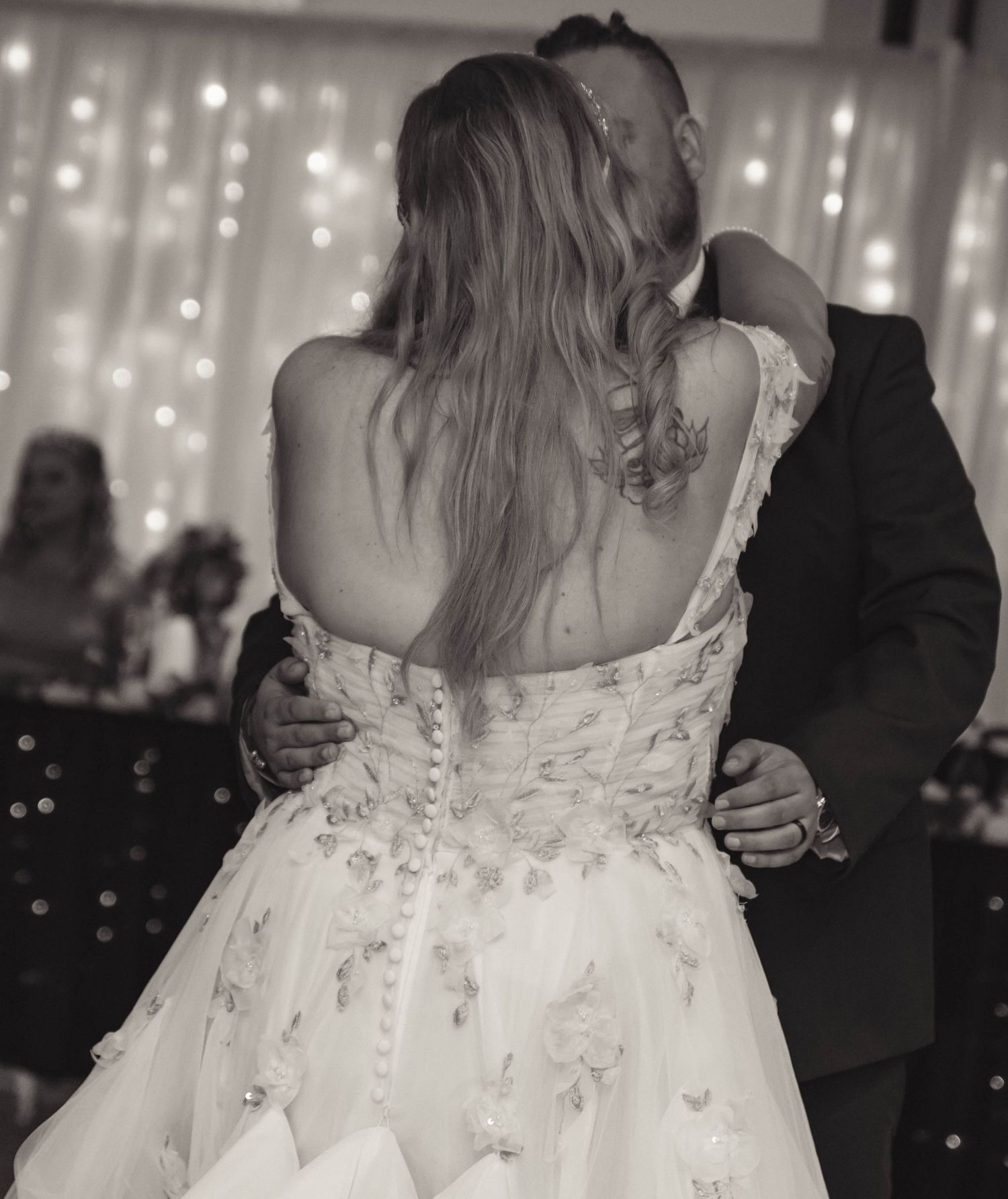 Black and white photo of couple sharing first dance, bride in floral wedding gown with button back detail.