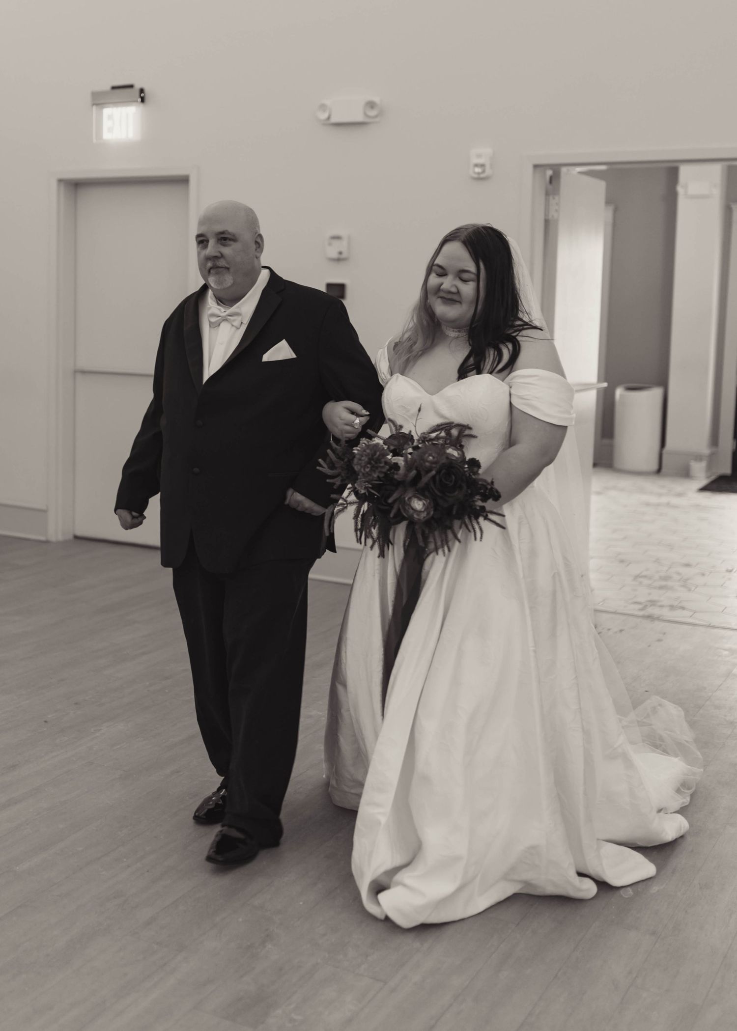 Black and white photo of bride walking with father down wedding aisle.