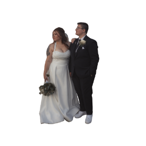 Bride in white gown holding bouquet stands beside groom in black suit with boutonniere at wedding ceremony.