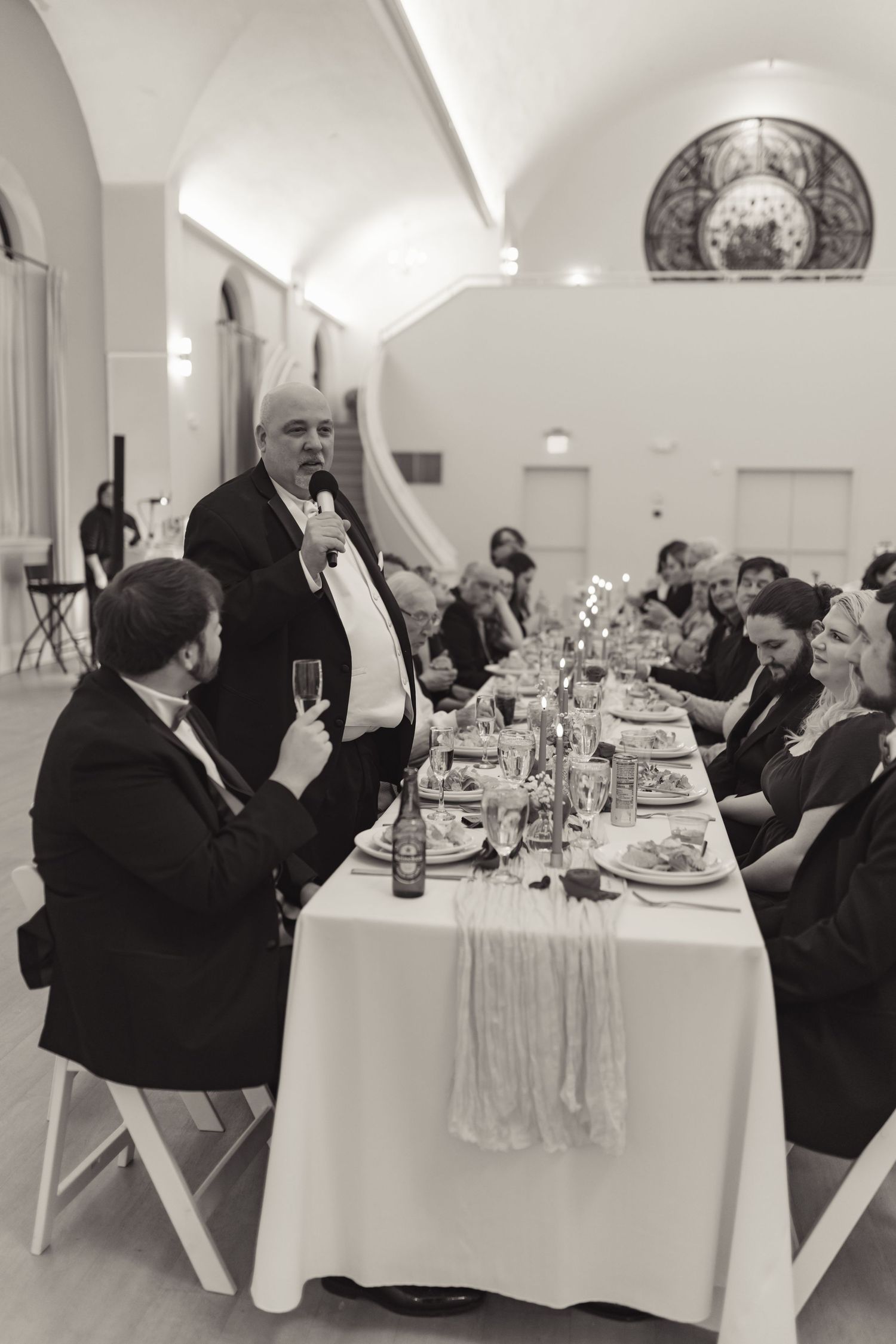 Man giving speech at formal dinner banquet table in black and white photo.