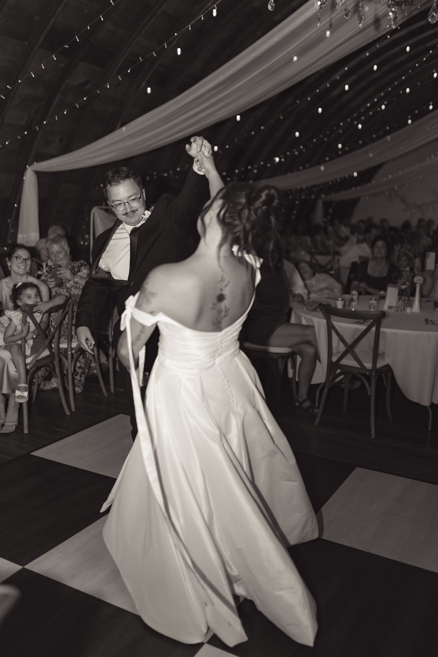 Black and white photo of bride and groom sharing first dance at elegant wedding reception venue.