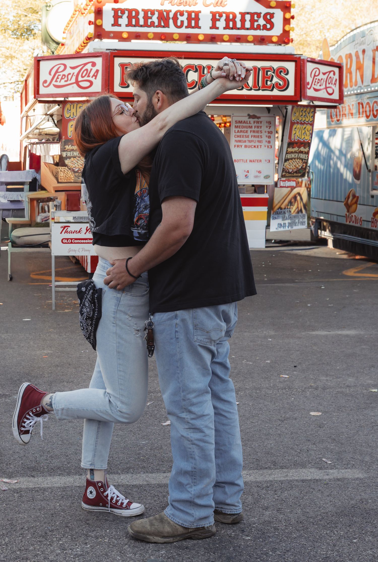 Couple sharing a romantic kiss at a carnival near a French Fries food stand.