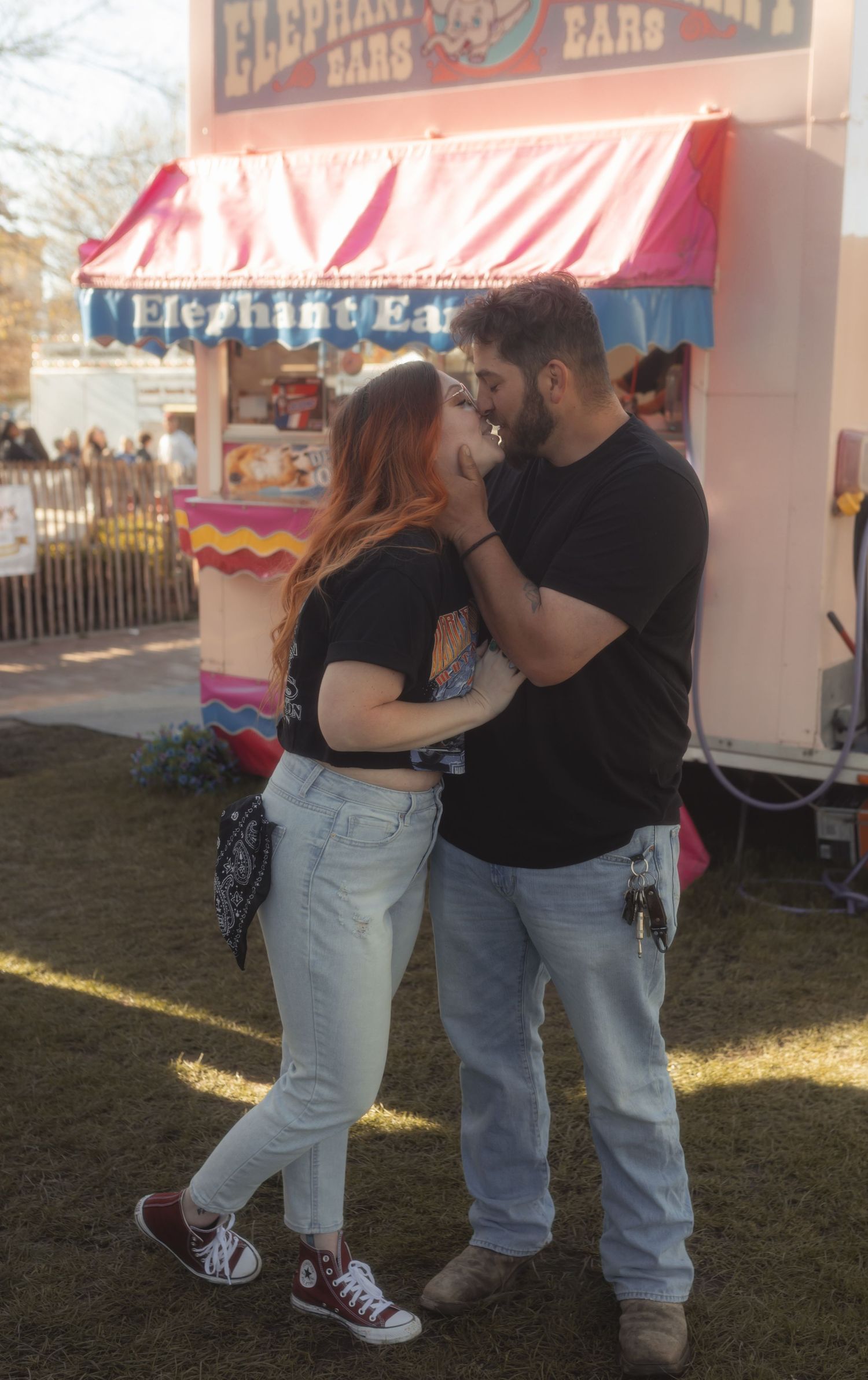 Couple sharing a romantic moment at a carnival fair near an Elephant Ears food stand outdoors.